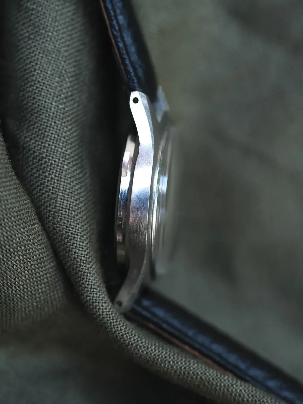 Vintage Omega watch side profile, stainless steel case, black leather strap on fabric