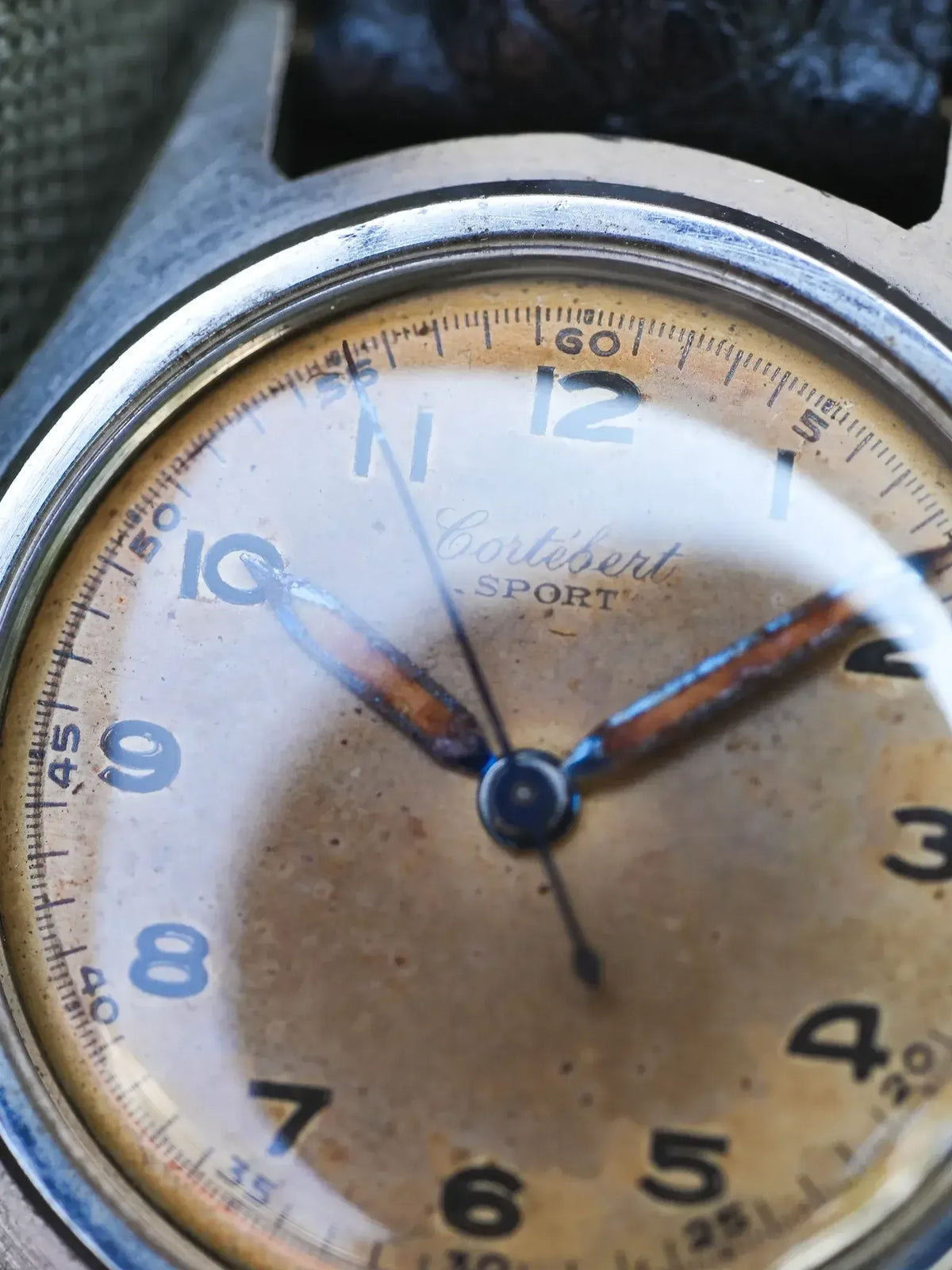 Vintage Cortébert Sport watch with aged cream dial, blue hands, and steel case