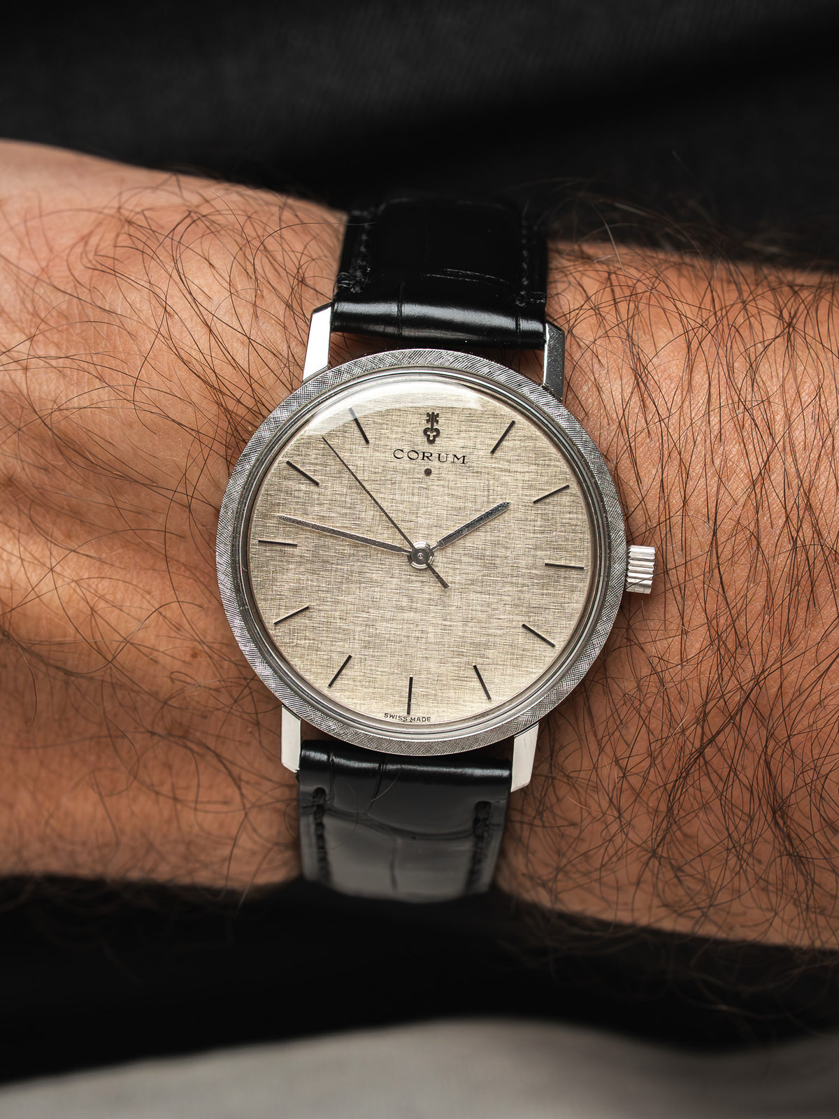 Montre Corum vintage, cadran texturé beige, bracelet cuir noir, portée au poignet