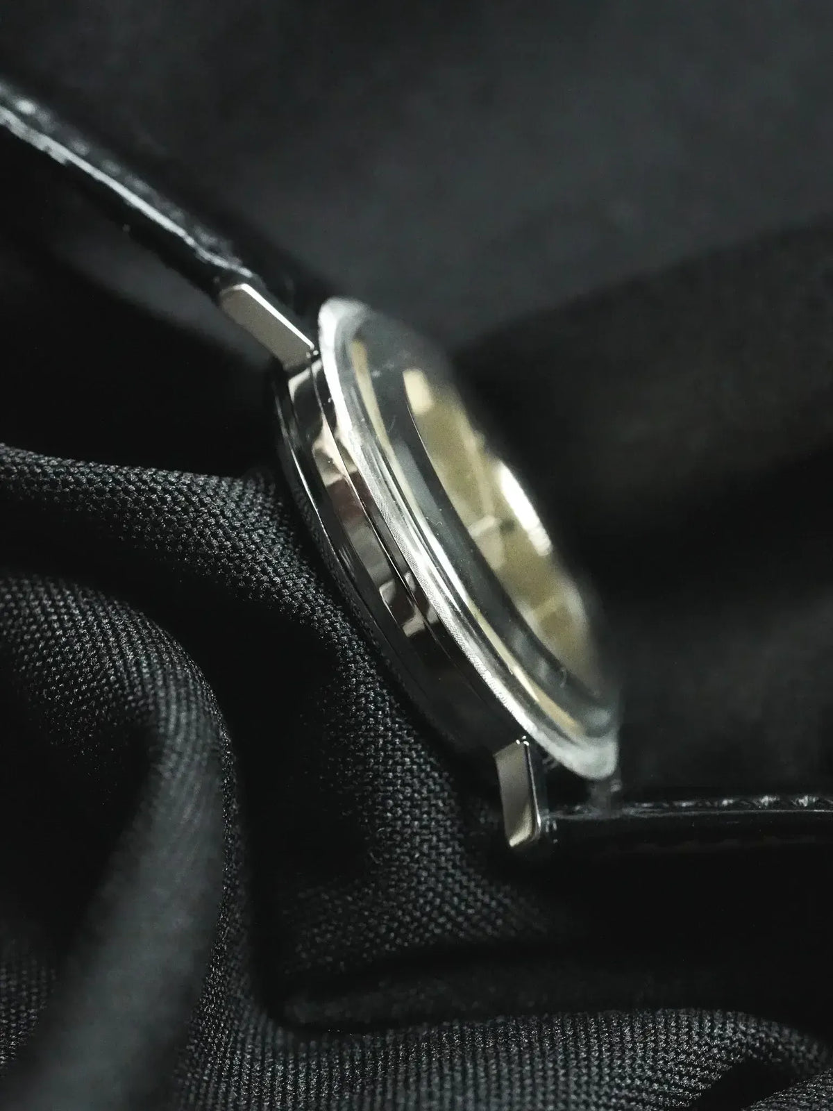 Vintage Omega watch with stainless steel case and black leather strap on dark fabric