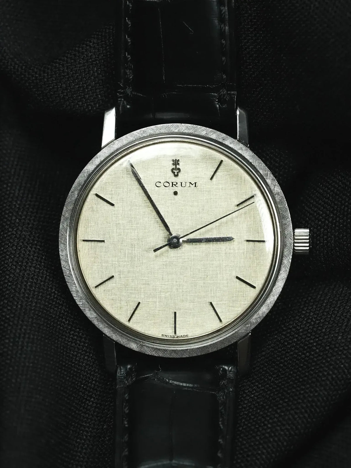 Vintage Corum watch with textured silver dial, black leather strap, and brushed steel case