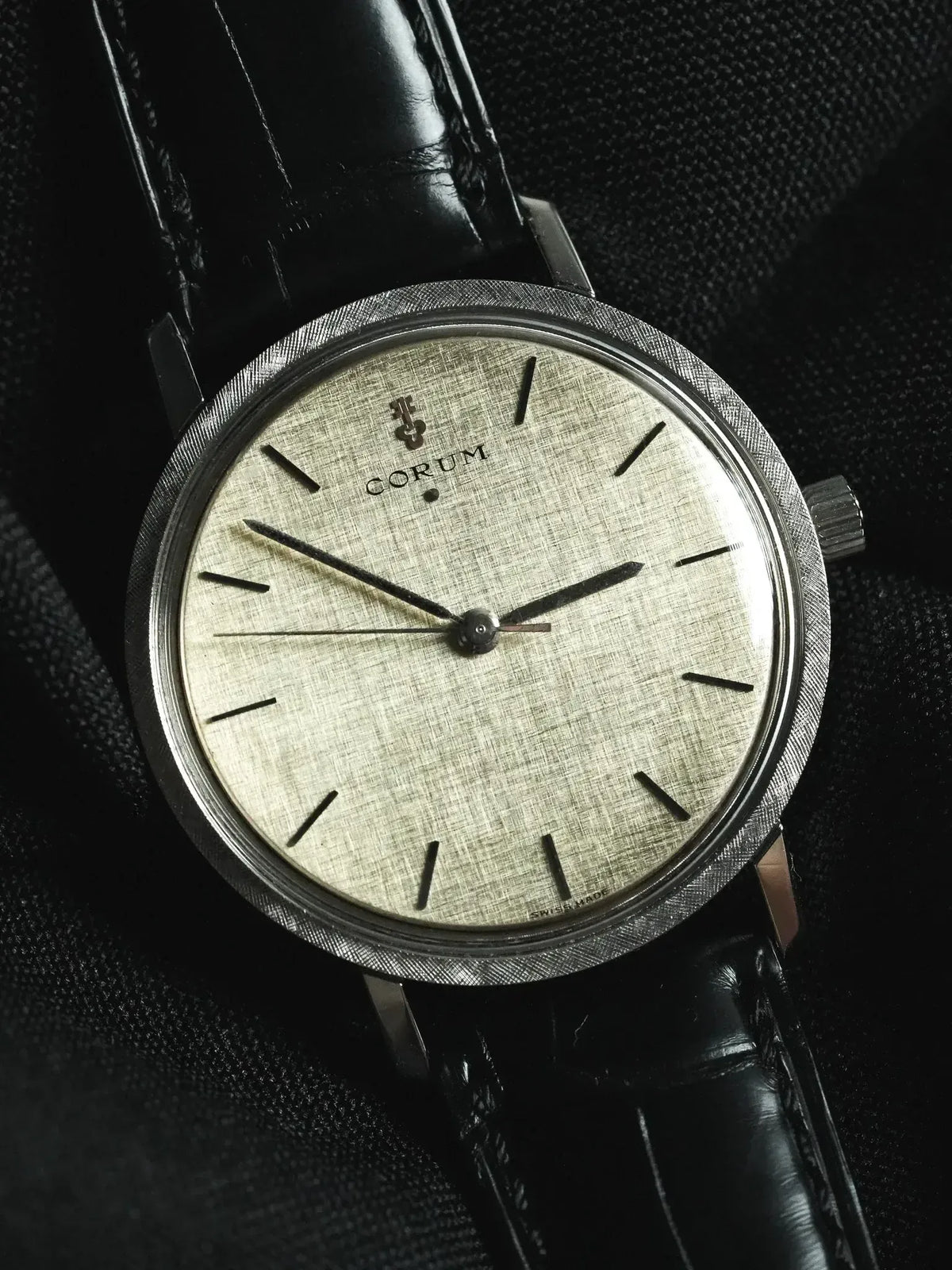 Corum vintage watch with textured silver dial, black leather strap, and brushed steel case