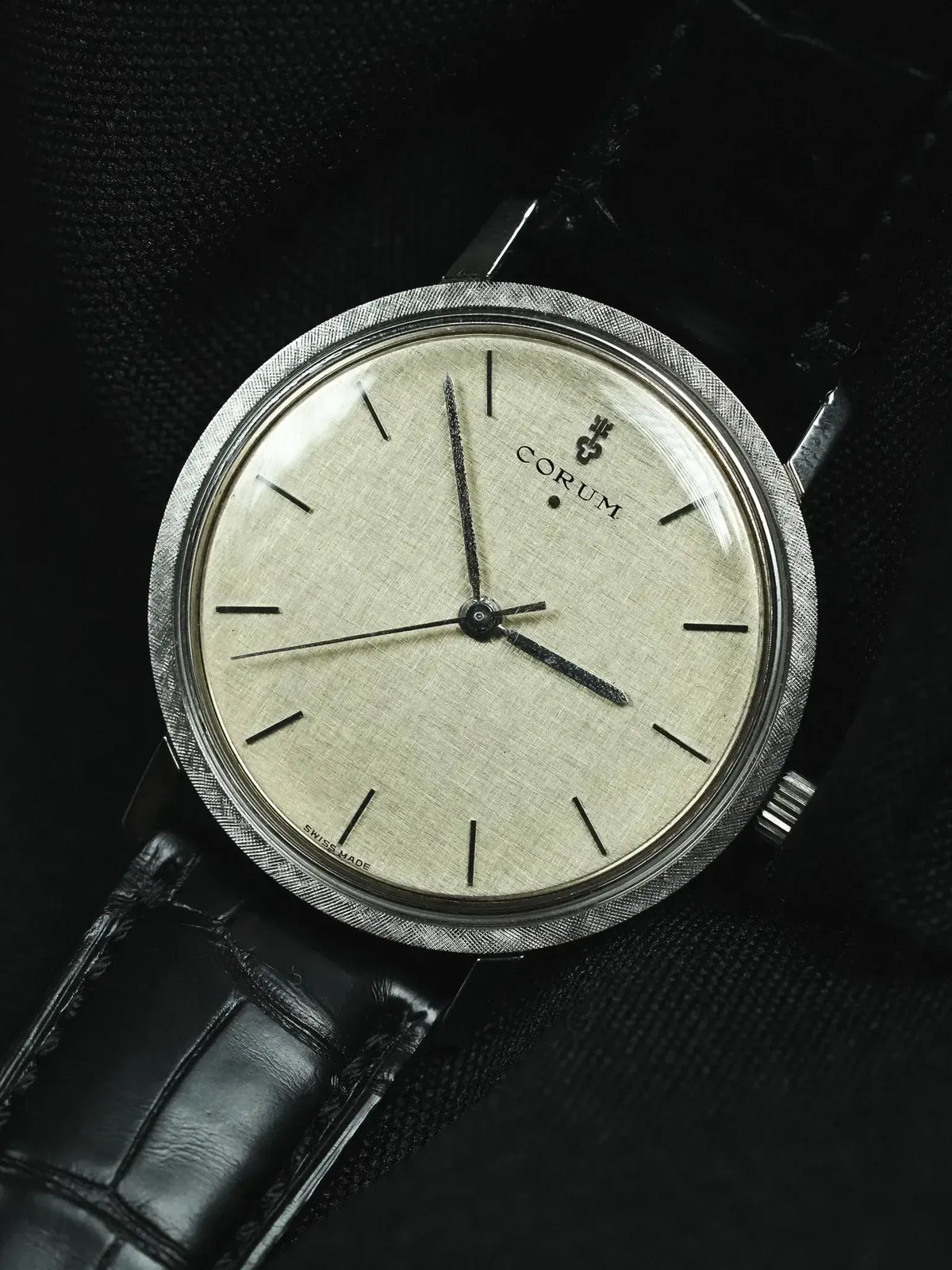Vintage Corum watch with textured silver dial, black leather strap, and brushed steel case