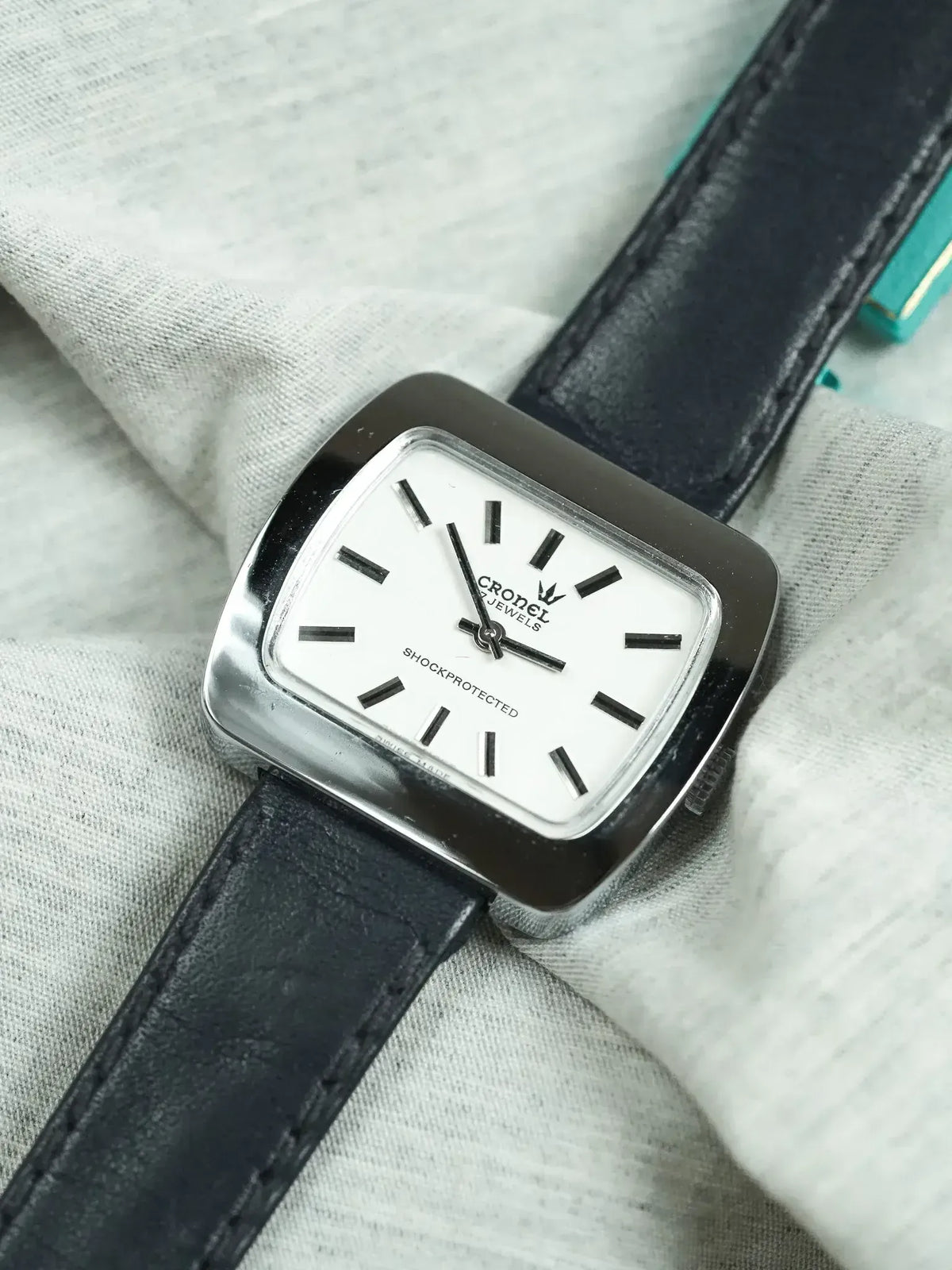 Cronel vintage watch with white dial, black leather strap, square case on fabric