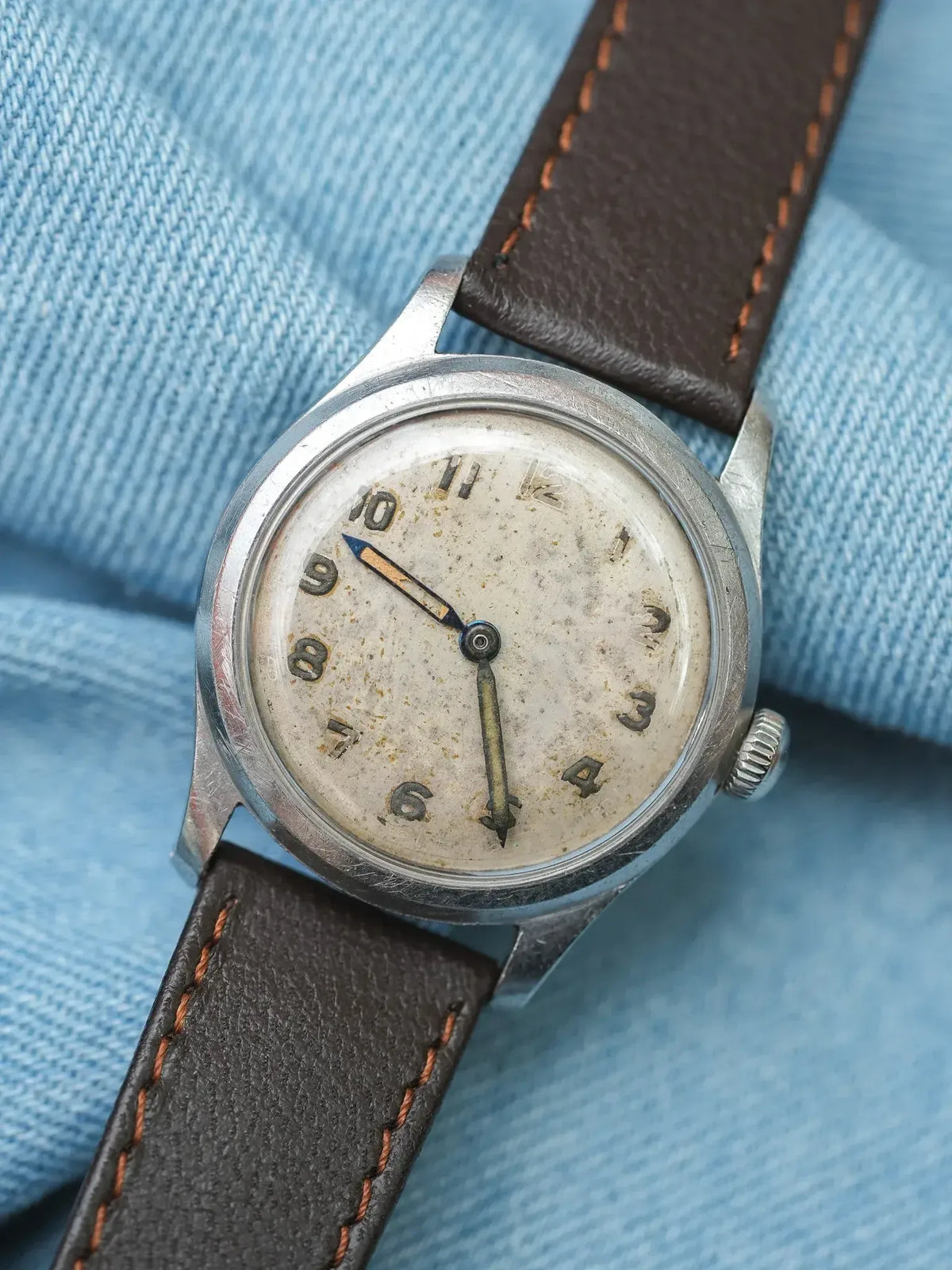 Vintage wristwatch with aged cream dial, steel case, brown leather strap on denim