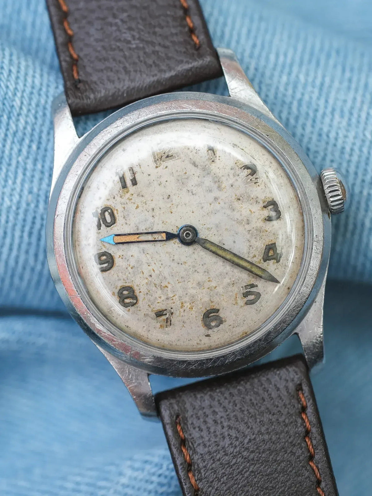Vintage watch with aged dial, steel case, brown leather strap on blue fabric