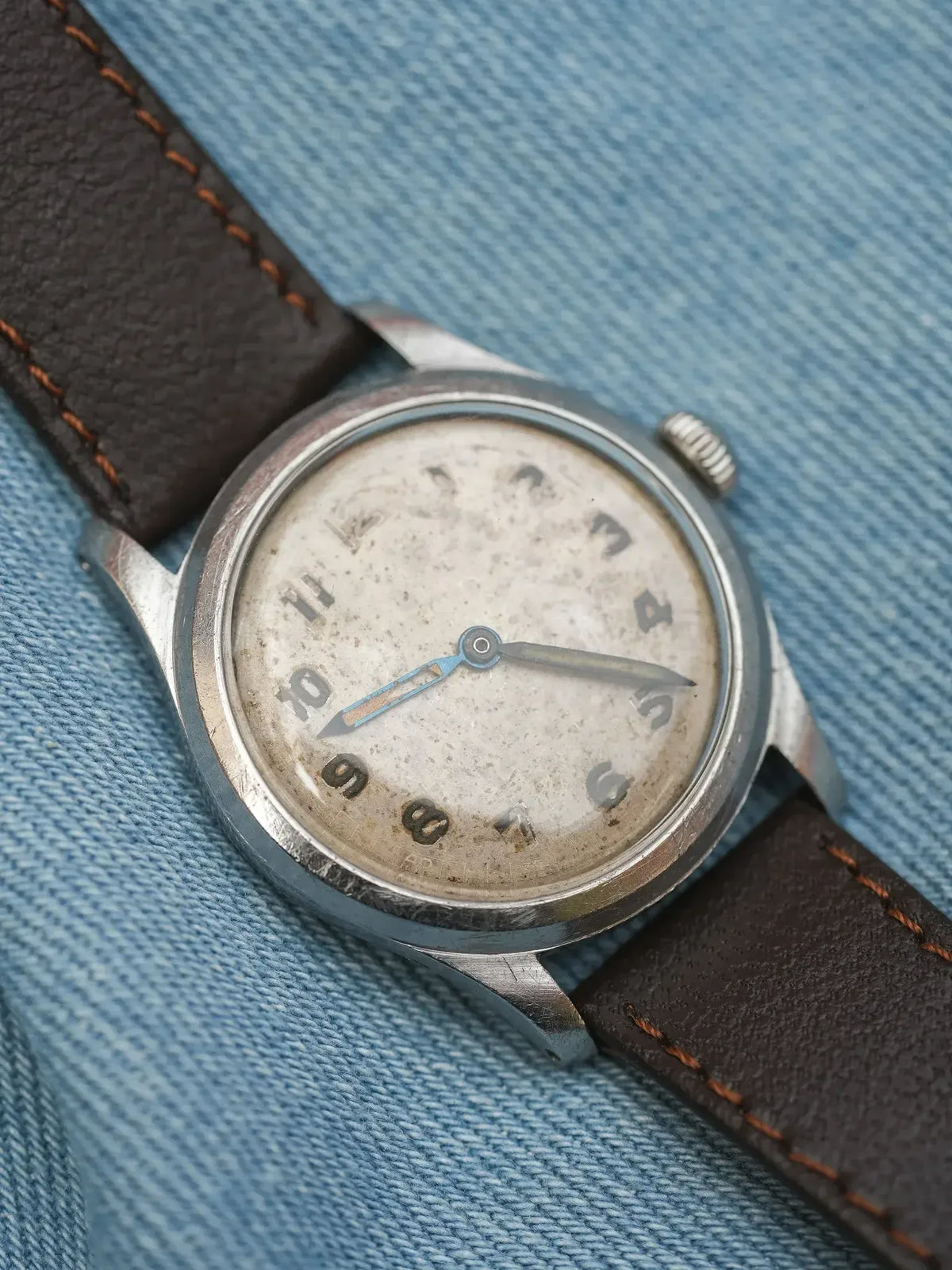 Vintage wristwatch with aged dial, steel case, brown leather strap on denim