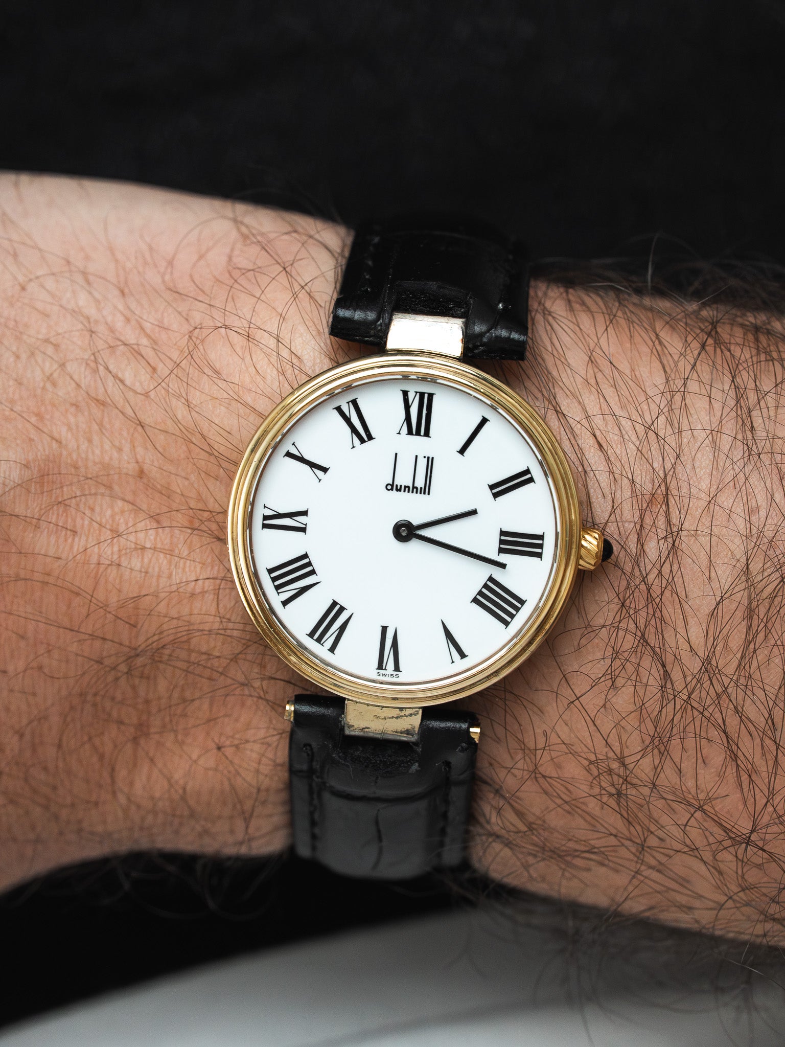 Dunhill vintage watch with gold case, white dial, Roman numerals, black leather strap on wrist