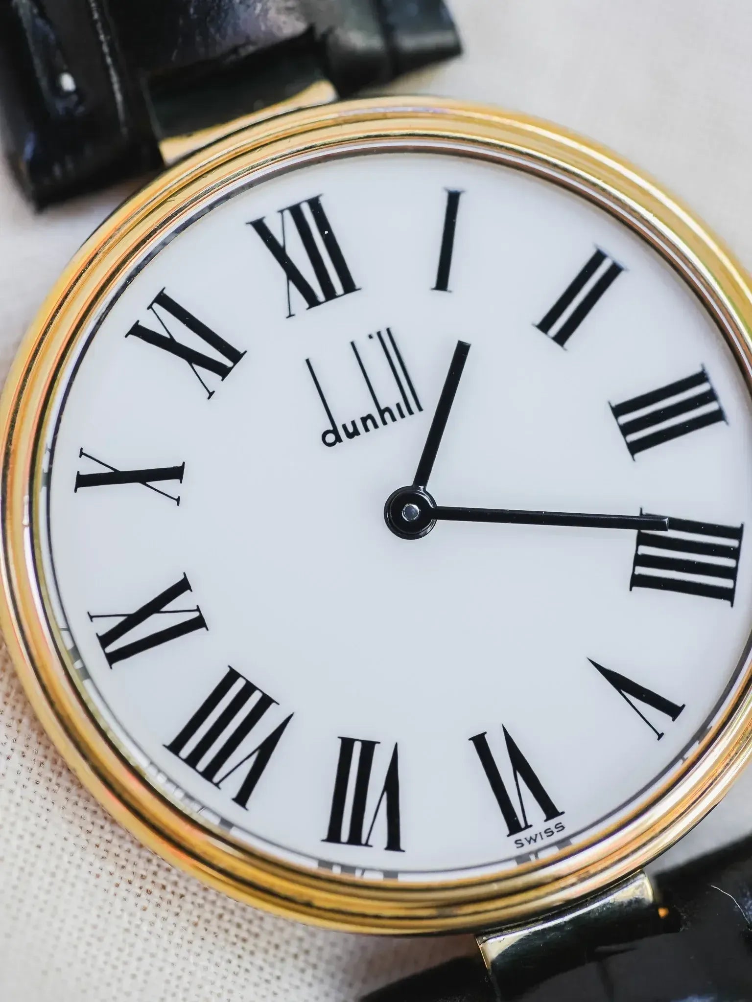 Dunhill vintage watch with gold case, white dial, black Roman numerals, and black leather strap
