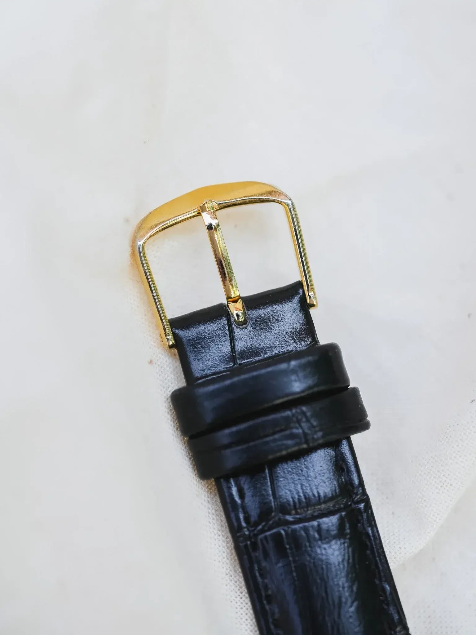 Black alligator leather watch strap with gold buckle on white background