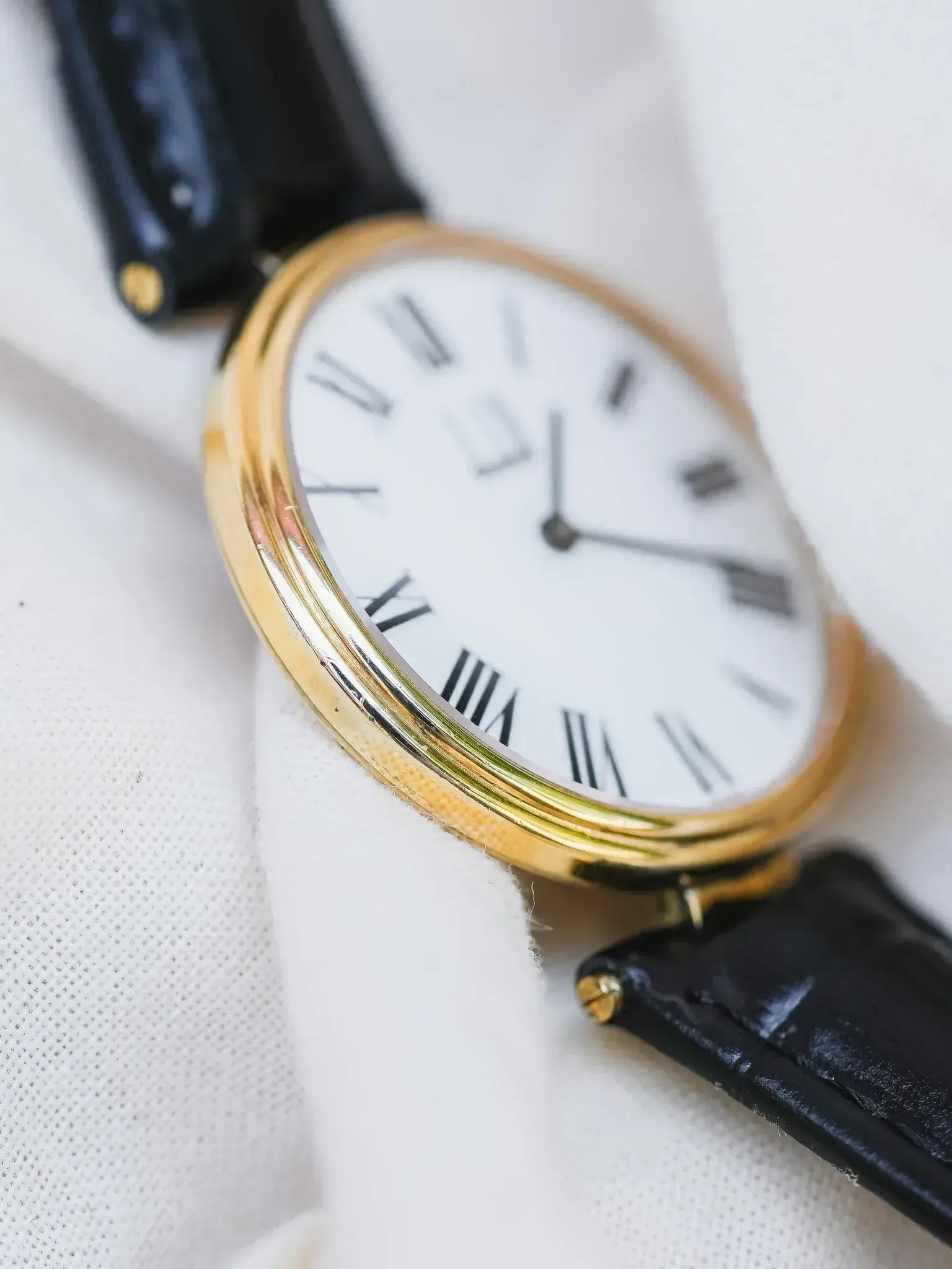 Vintage Cartier watch with gold case, white dial, Roman numerals, black leather strap