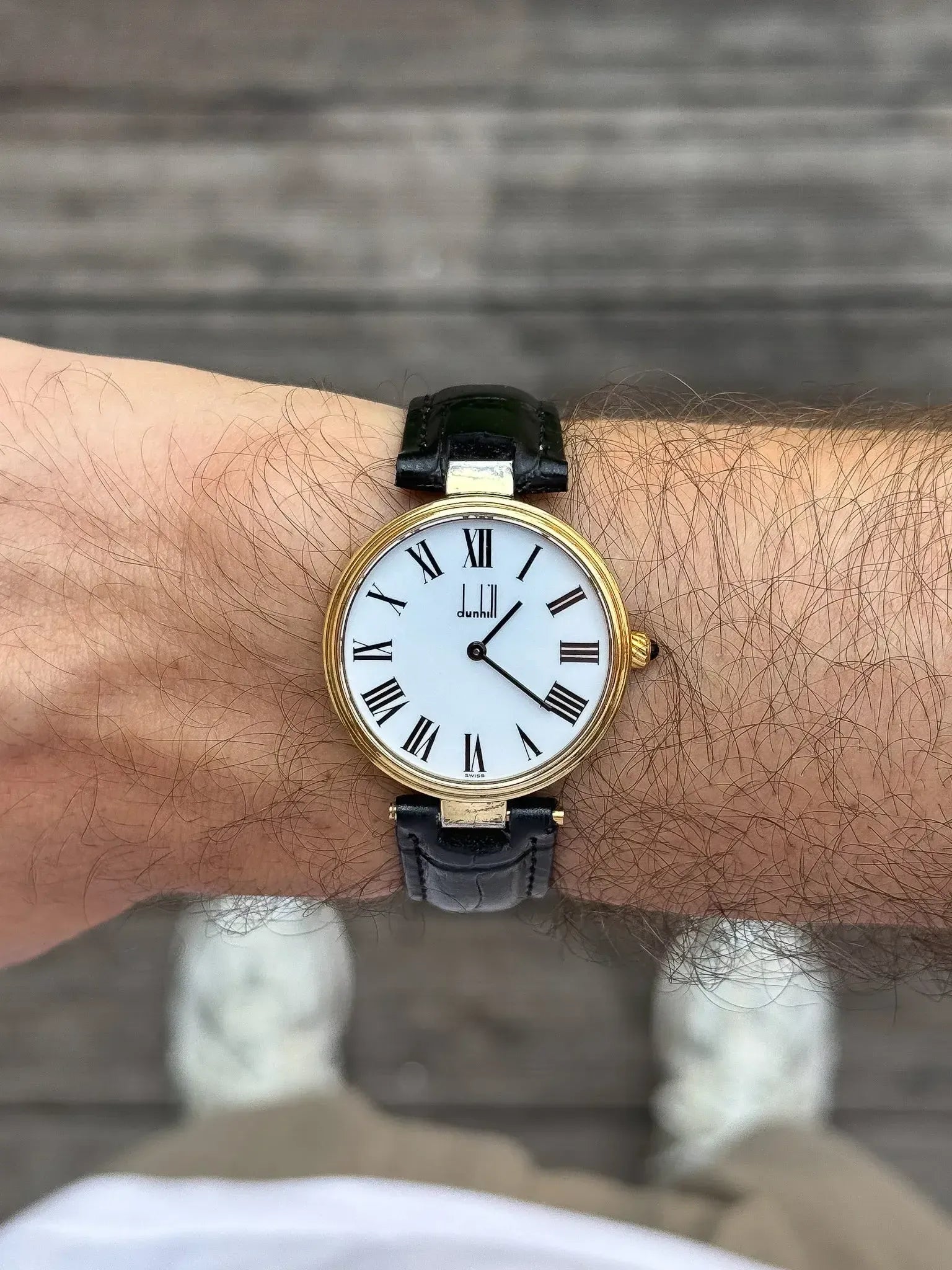 Dunhill vintage watch with gold case, white dial, Roman numerals, black leather strap on wrist