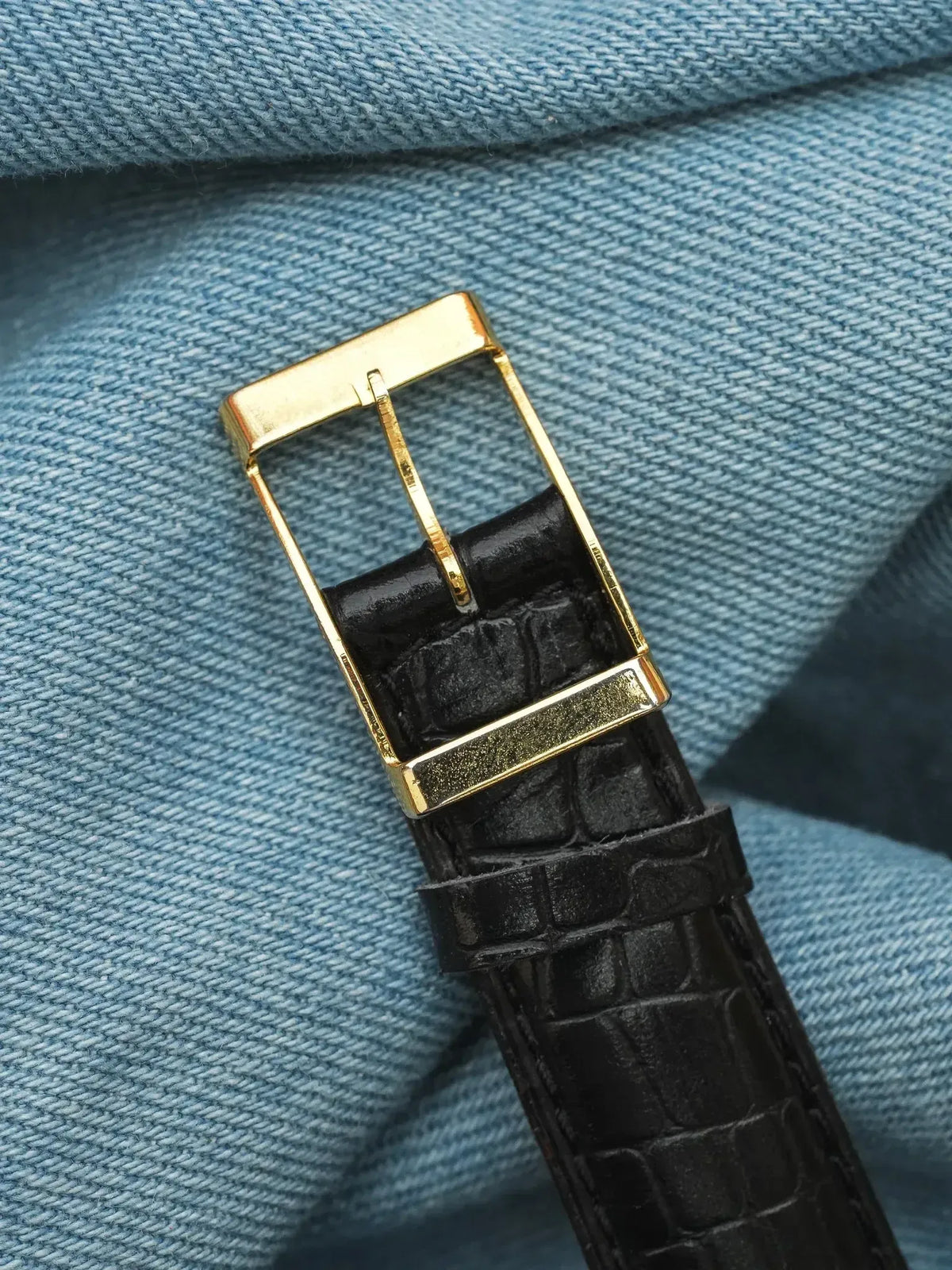 Black alligator leather watch strap with gold buckle on denim background