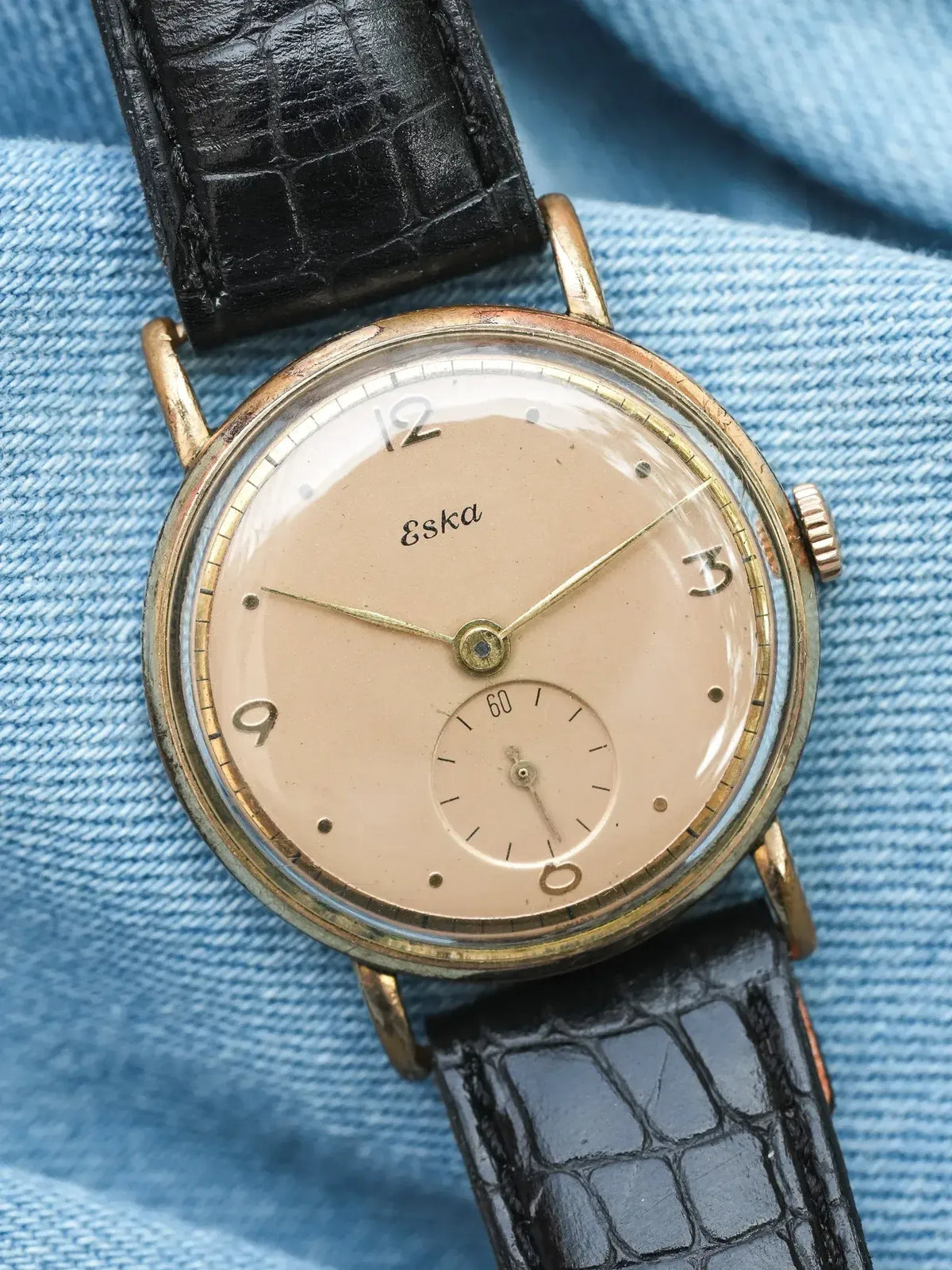 Vintage Eska watch with cream dial, gold case, black crocodile strap on denim