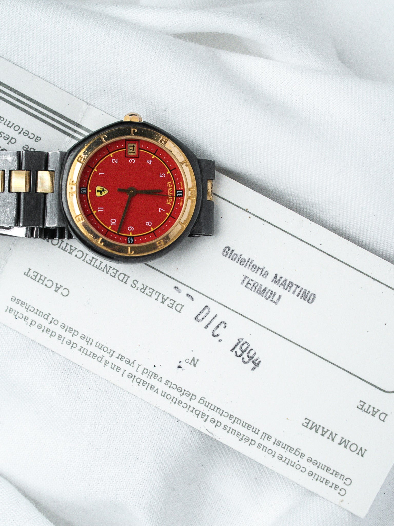 Ferrari vintage watch with red dial, gold bezel, and two-tone bracelet on document
