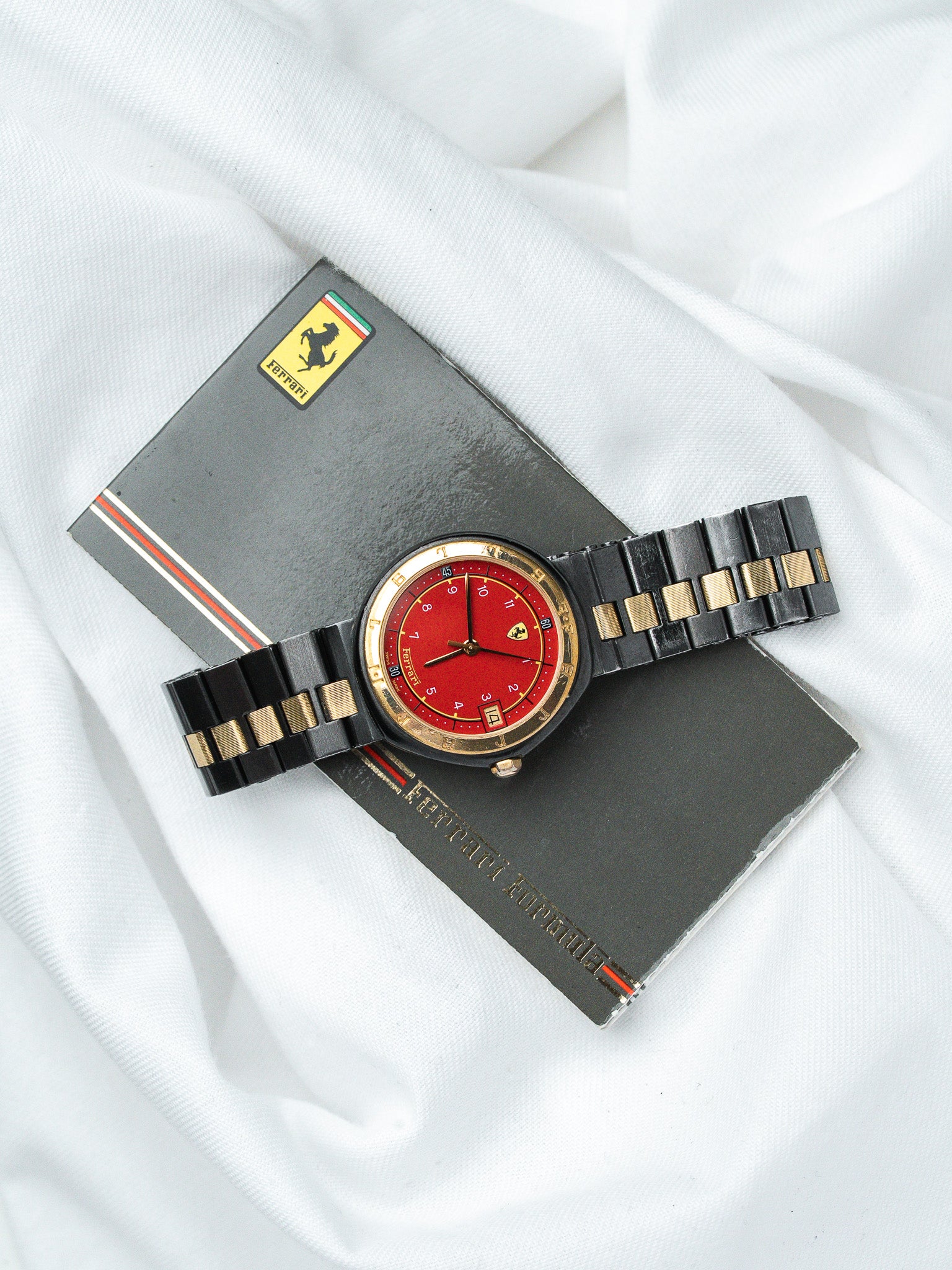 Ferrari vintage watch with red dial, black and gold bracelet, resting on Ferrari booklet