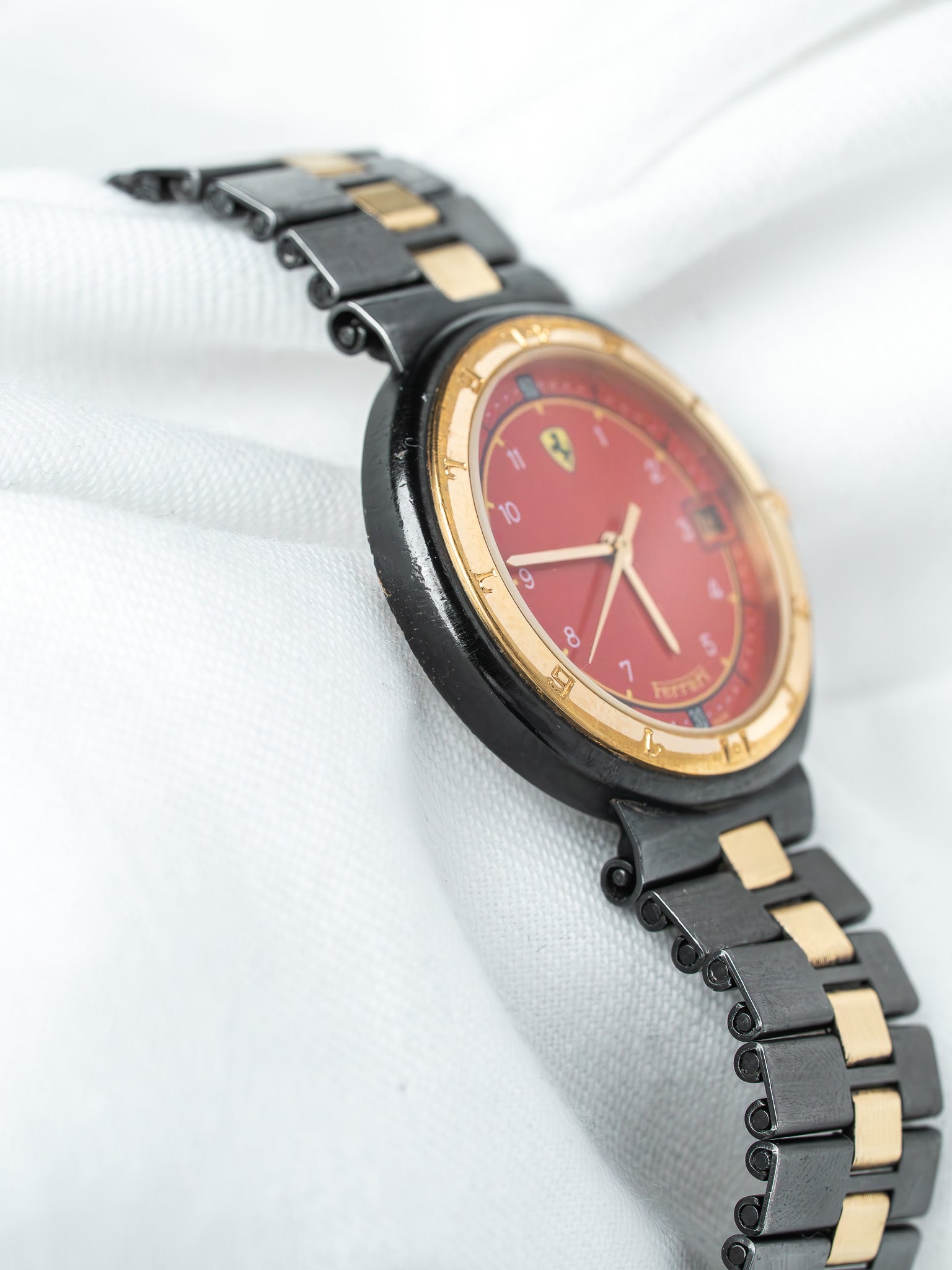 Ferrari vintage watch with red dial, gold accents, black bracelet on white fabric
