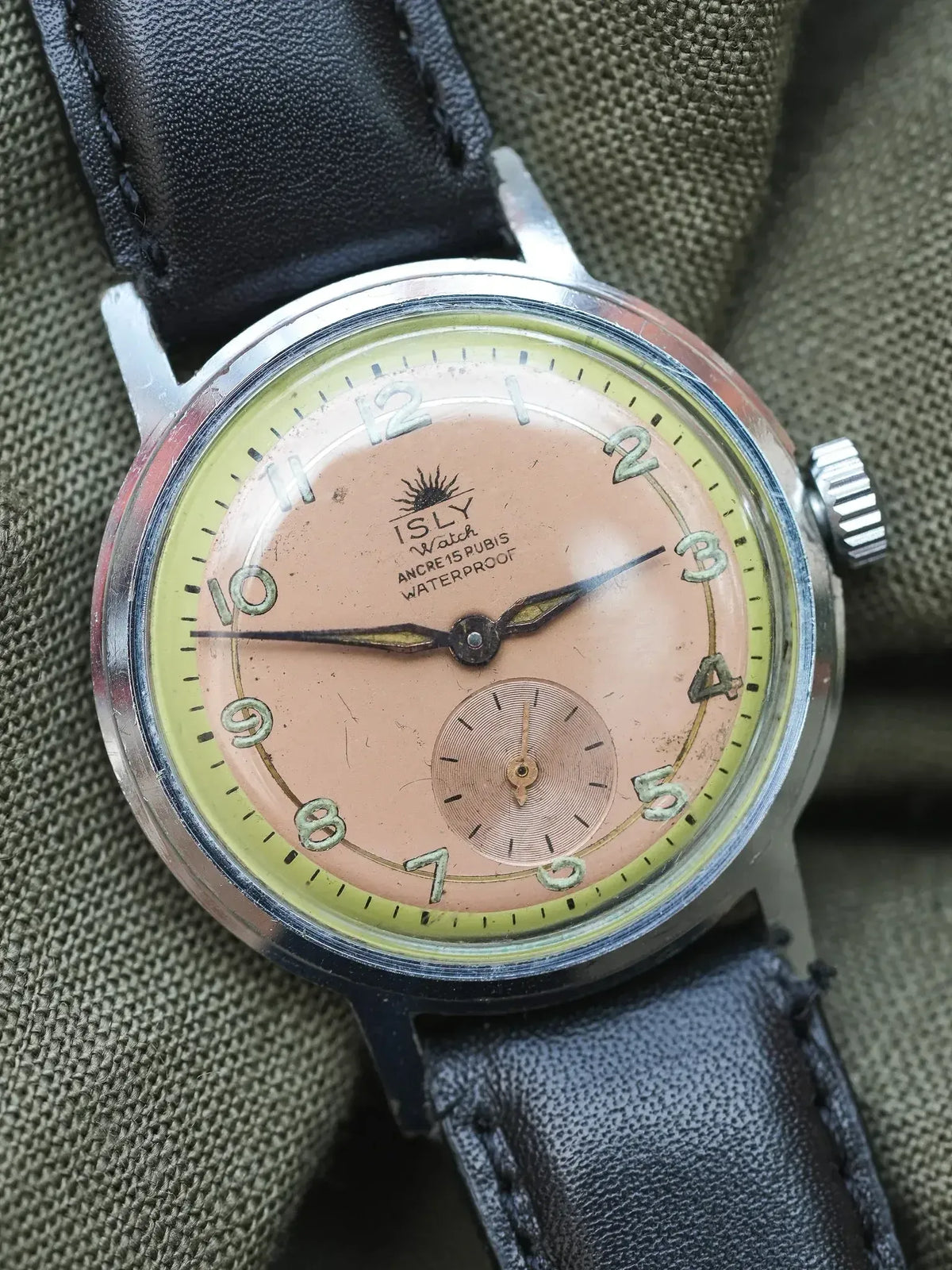 ISLY vintage watch with pink dial, yellow bezel, black leather strap on fabric background
