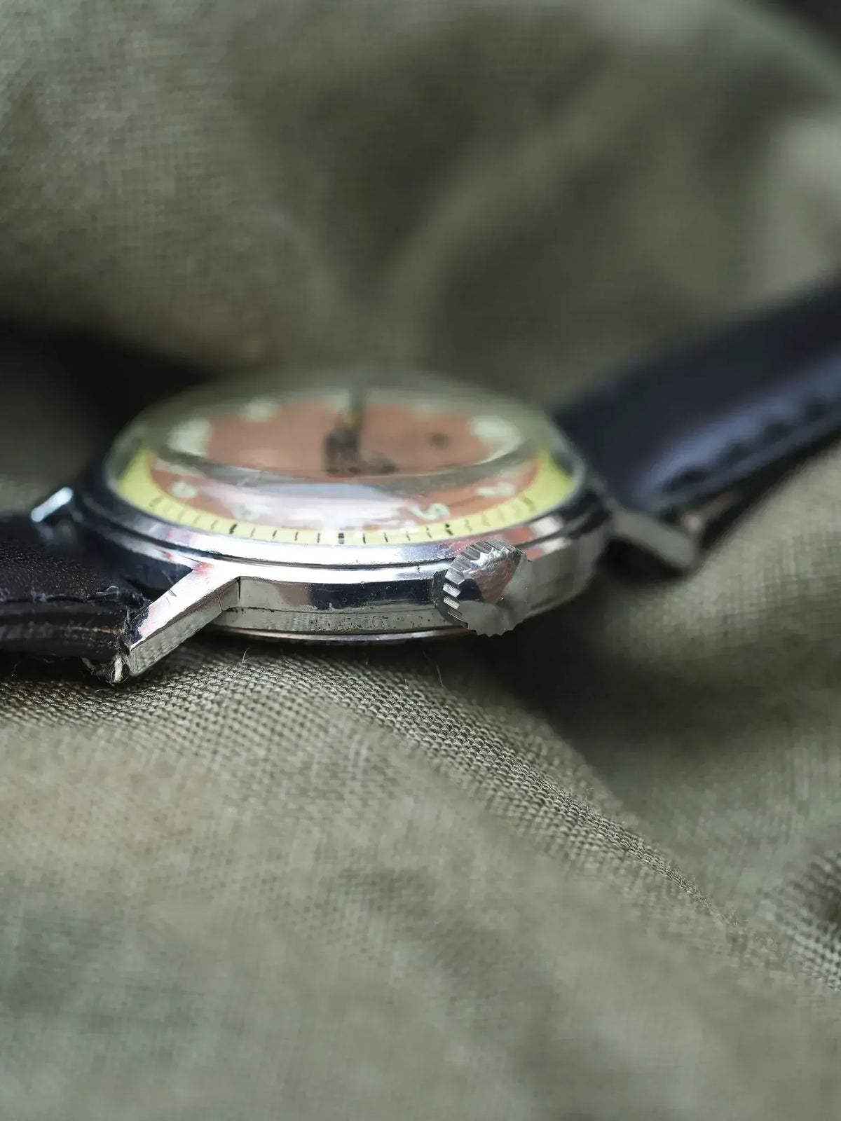 Vintage watch with silver case, faded dial, black leather strap on fabric