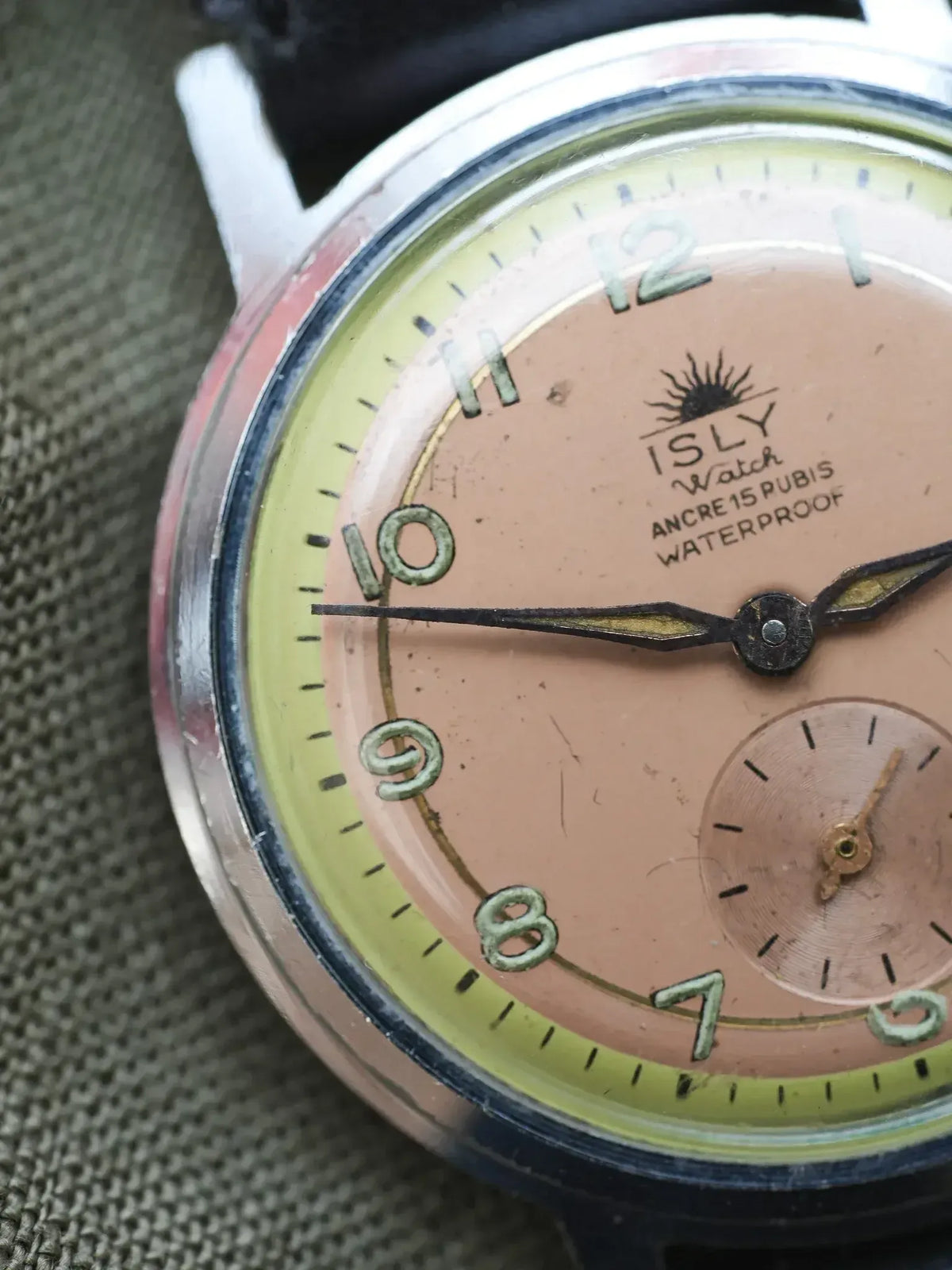 ISLY vintage watch with pink dial, green numerals, and steel case on fabric