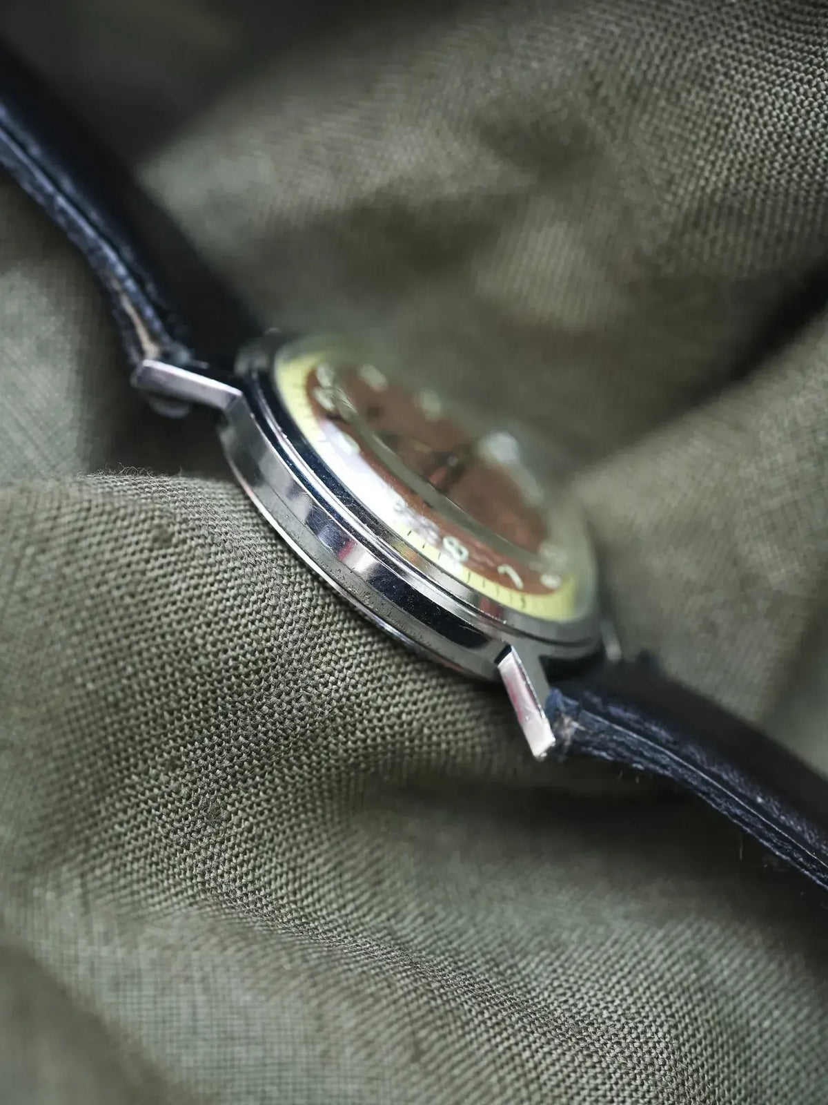Vintage Omega watch with brown dial, steel case, black leather strap on olive fabric