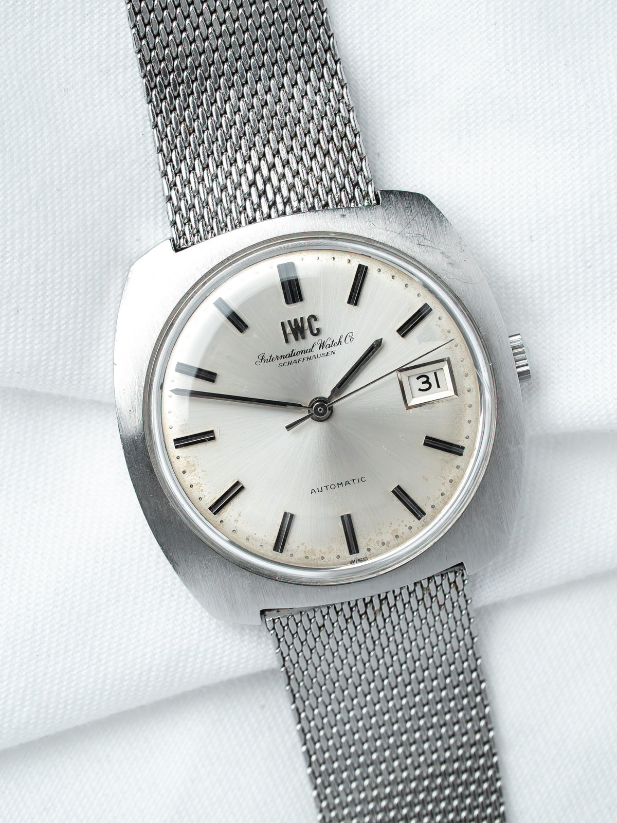 IWC vintage automatic watch with silver dial, black markers, and mesh bracelet on white fabric