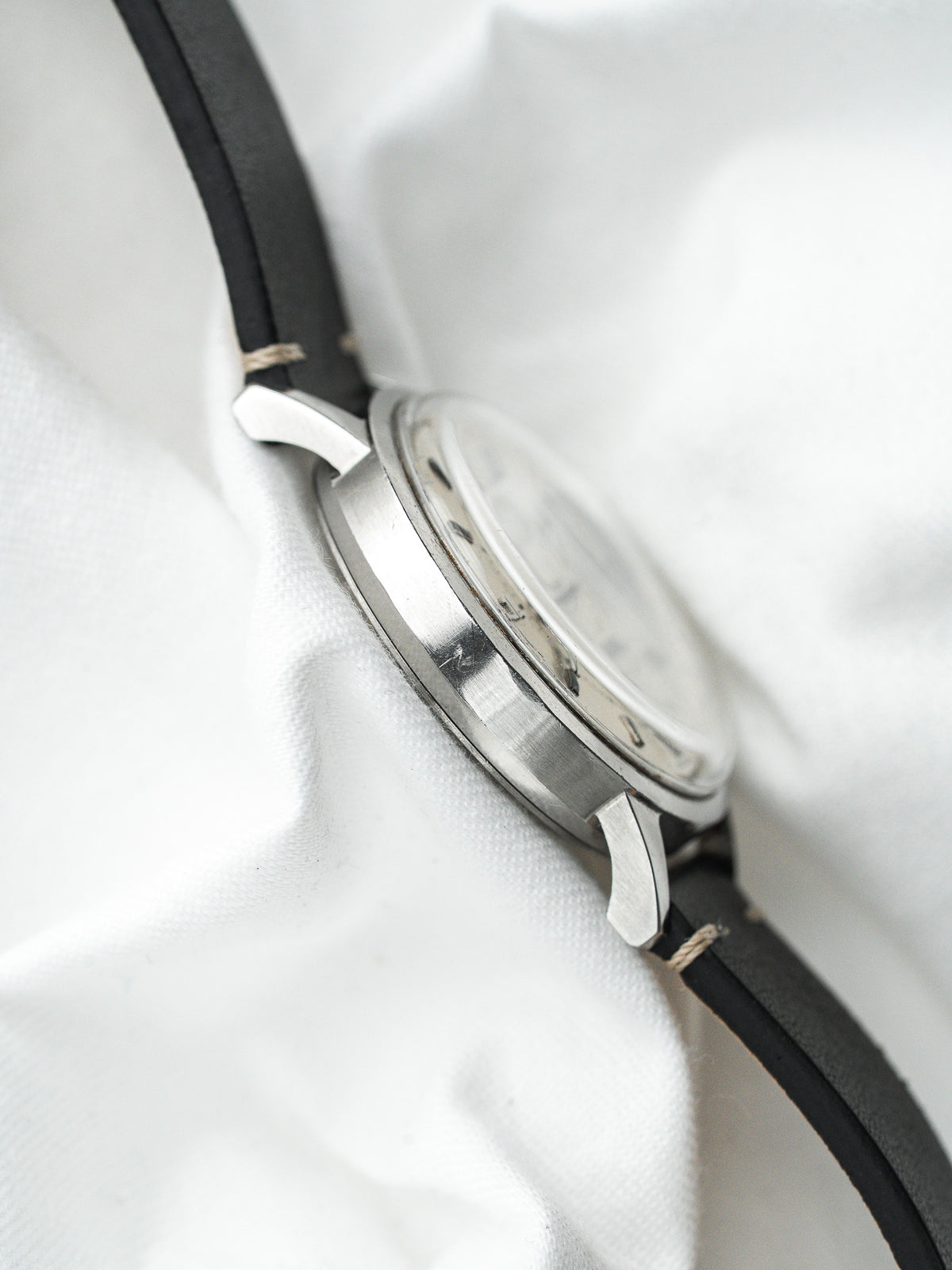 Vintage Watch aus Stahl mit schwarzem Lederarmband auf einem zerknitterten weißen Hintergrund