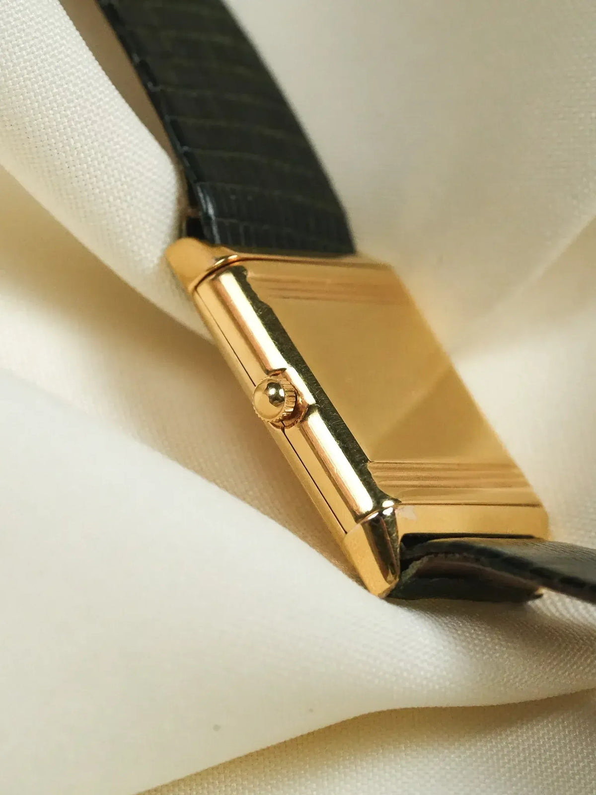 Cartier Tank vintage watch with gold case and black leather strap on white fabric