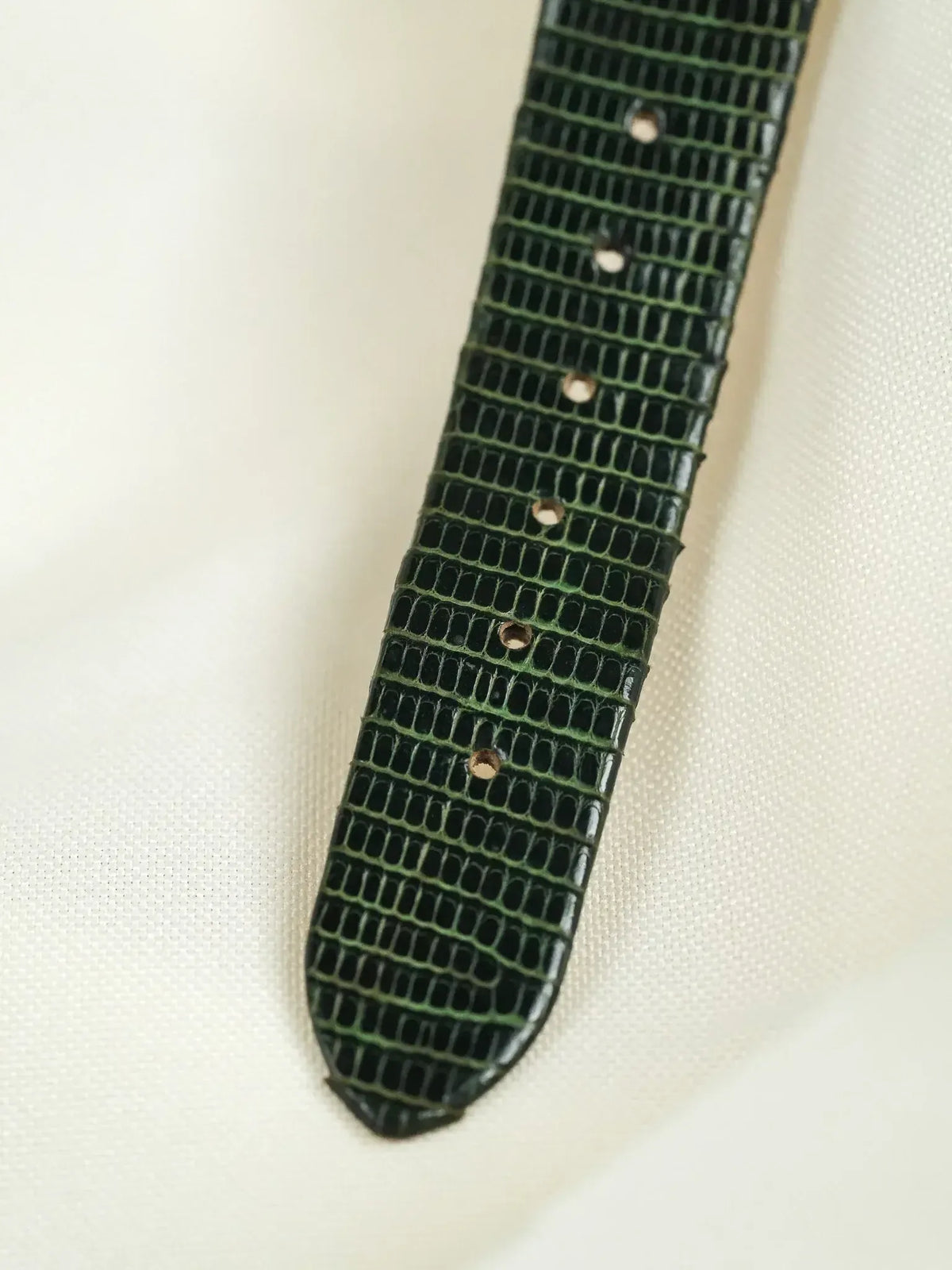 Green alligator leather watch strap with gold tone holes on white fabric