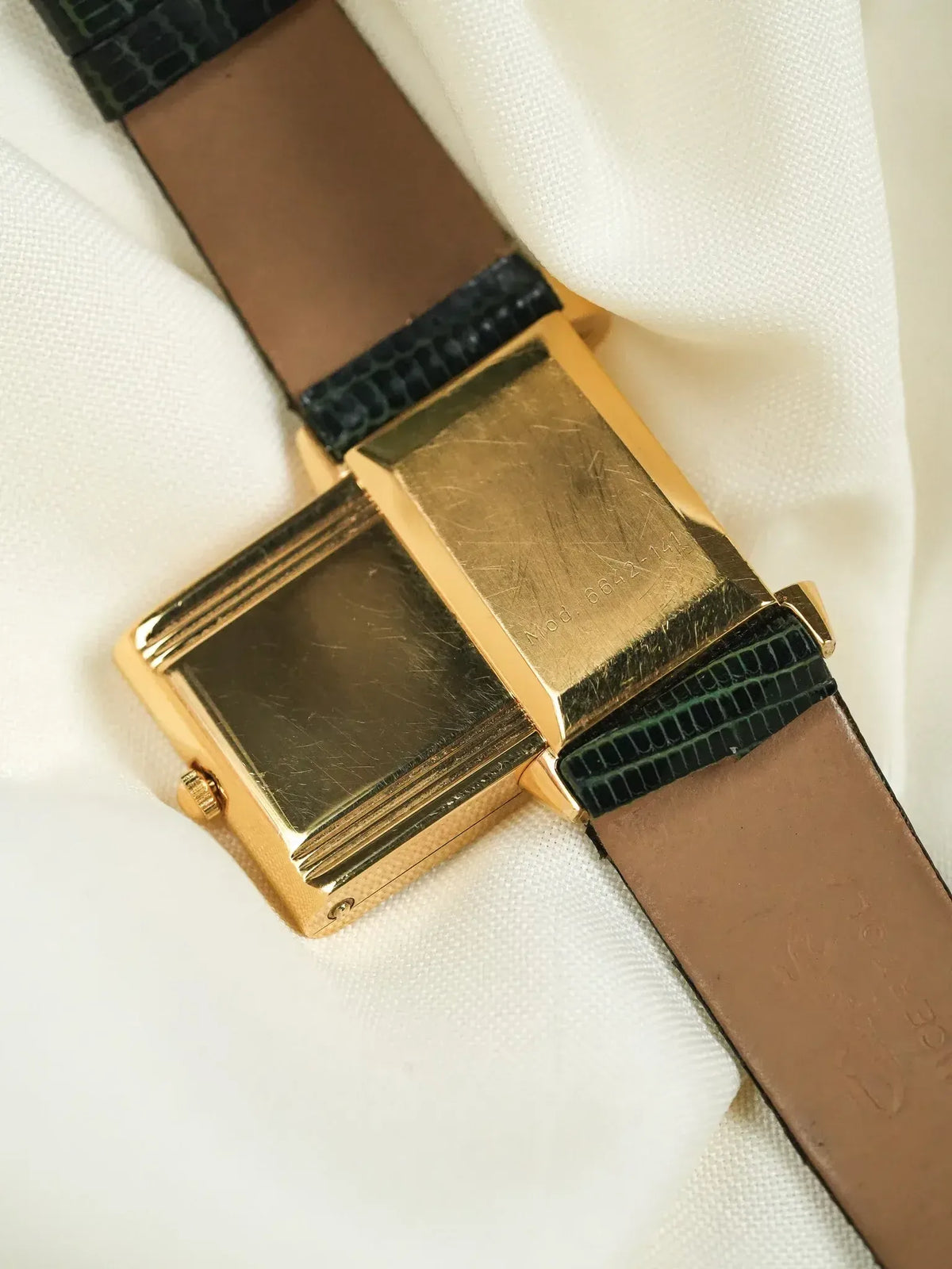 Vintage Universal Genève rectangular gold watch with black lizard strap on white fabric