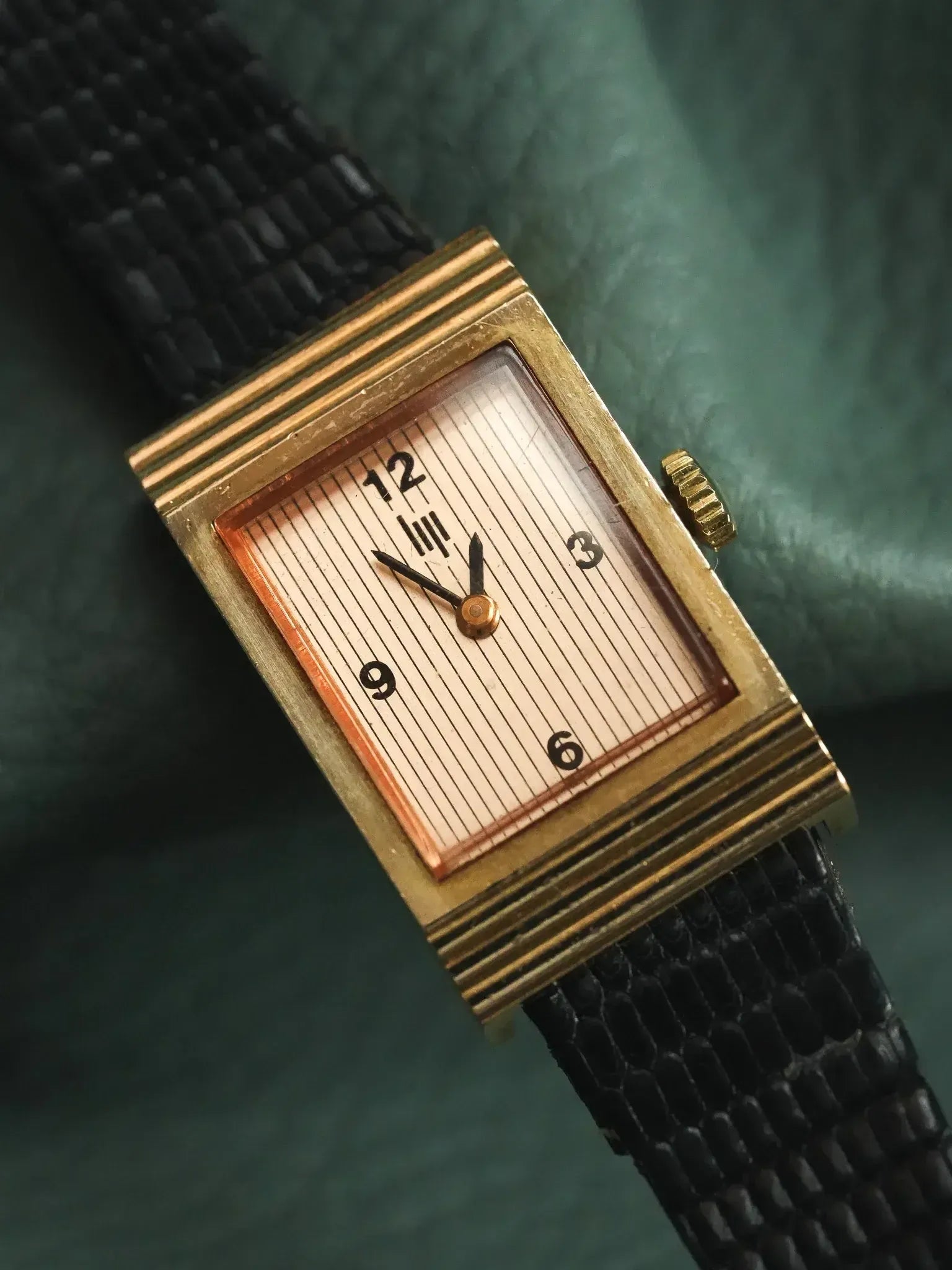 Vintage rectangular gold watch with striped dial, black textured strap on green fabric