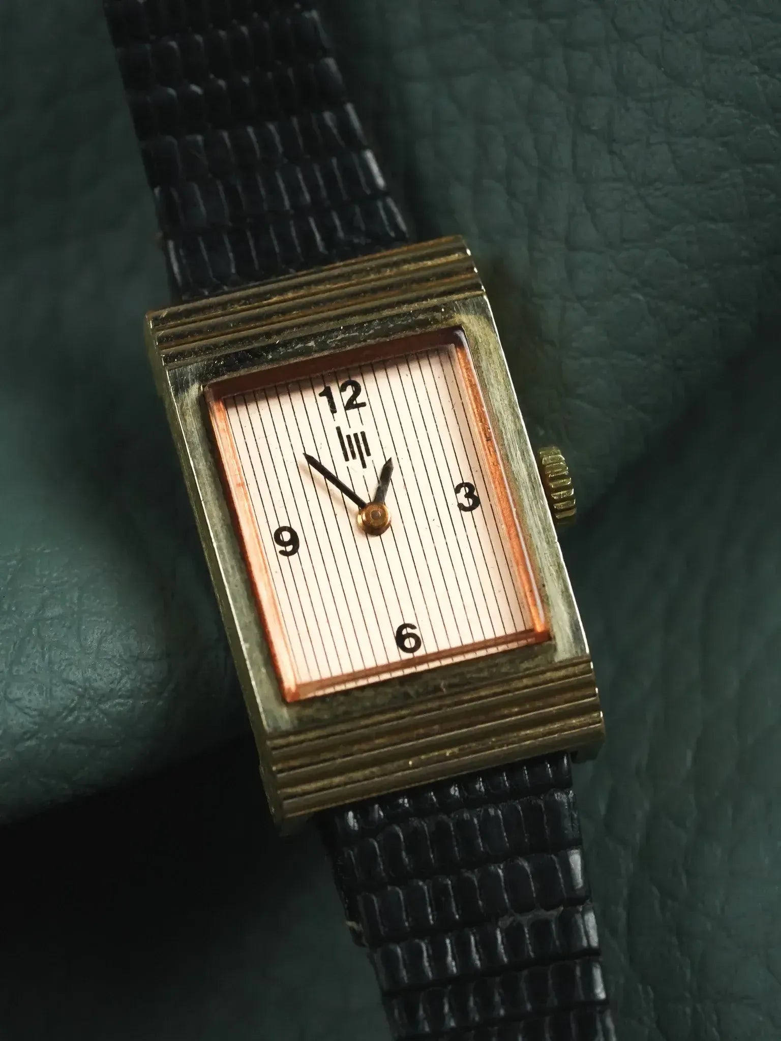 Vintage rectangular gold watch with striped dial, black leather strap on green leather