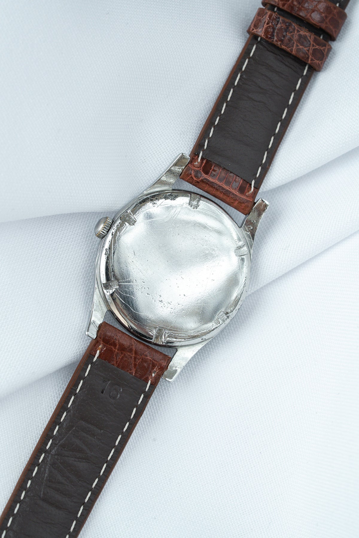 Vintage watch with stainless steel case and brown leather strap, back view on white fabric