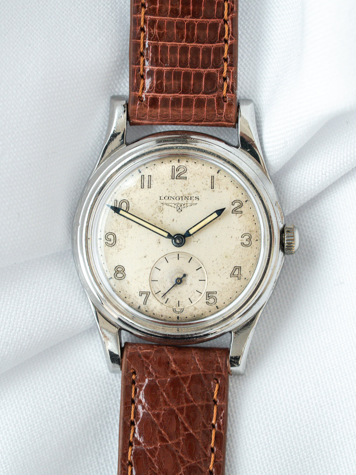 Vintage Longines watch with cream dial, steel case, brown leather strap on white fabric