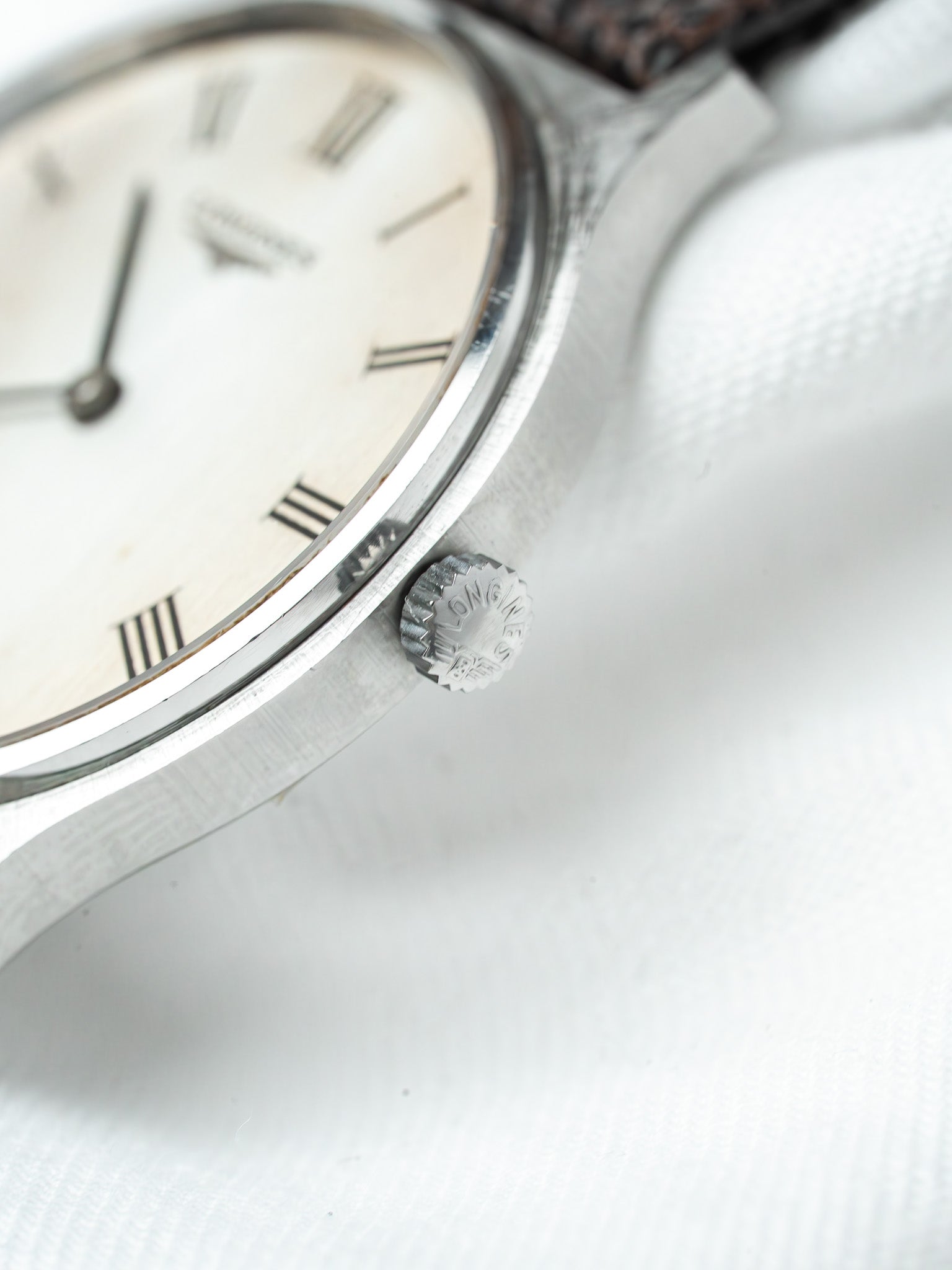 Vintage Longines watch with silver case, cream dial, Roman numerals, and brown leather strap