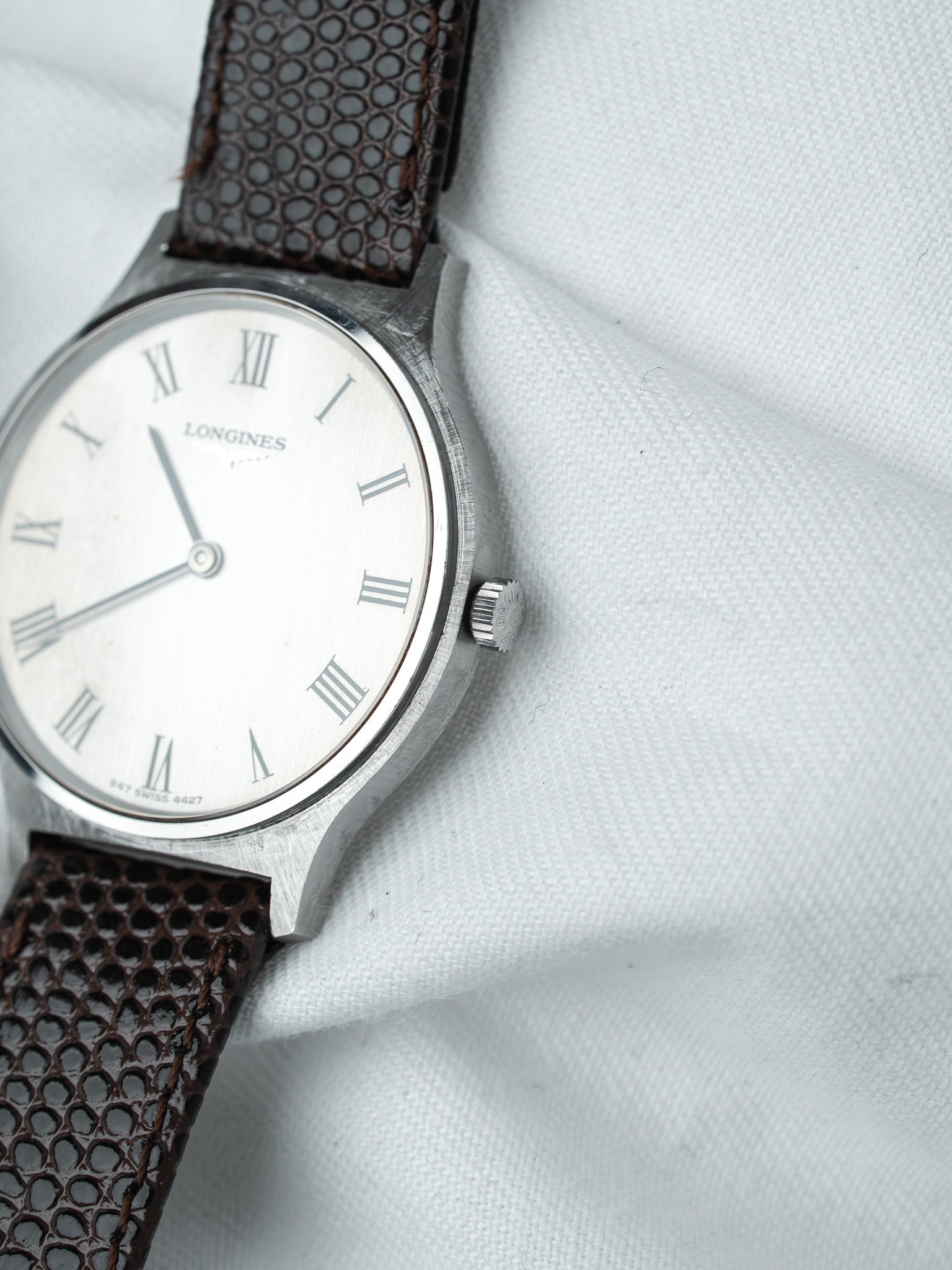Longines vintage watch with silver dial, Roman numerals, brown textured strap on white fabric