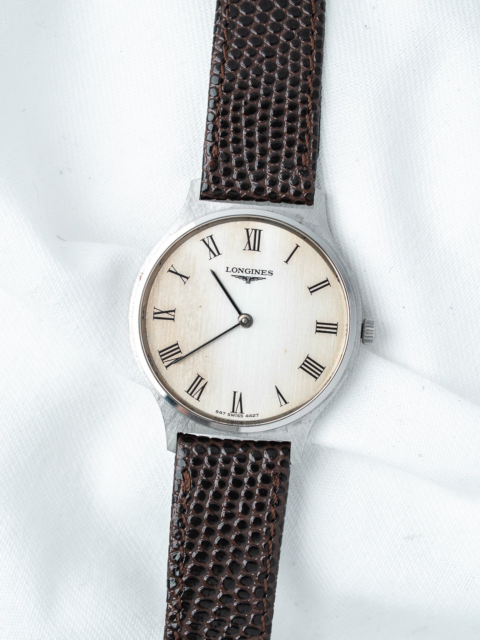 Longines vintage watch with silver case, cream dial, Roman numerals, brown textured strap on white background