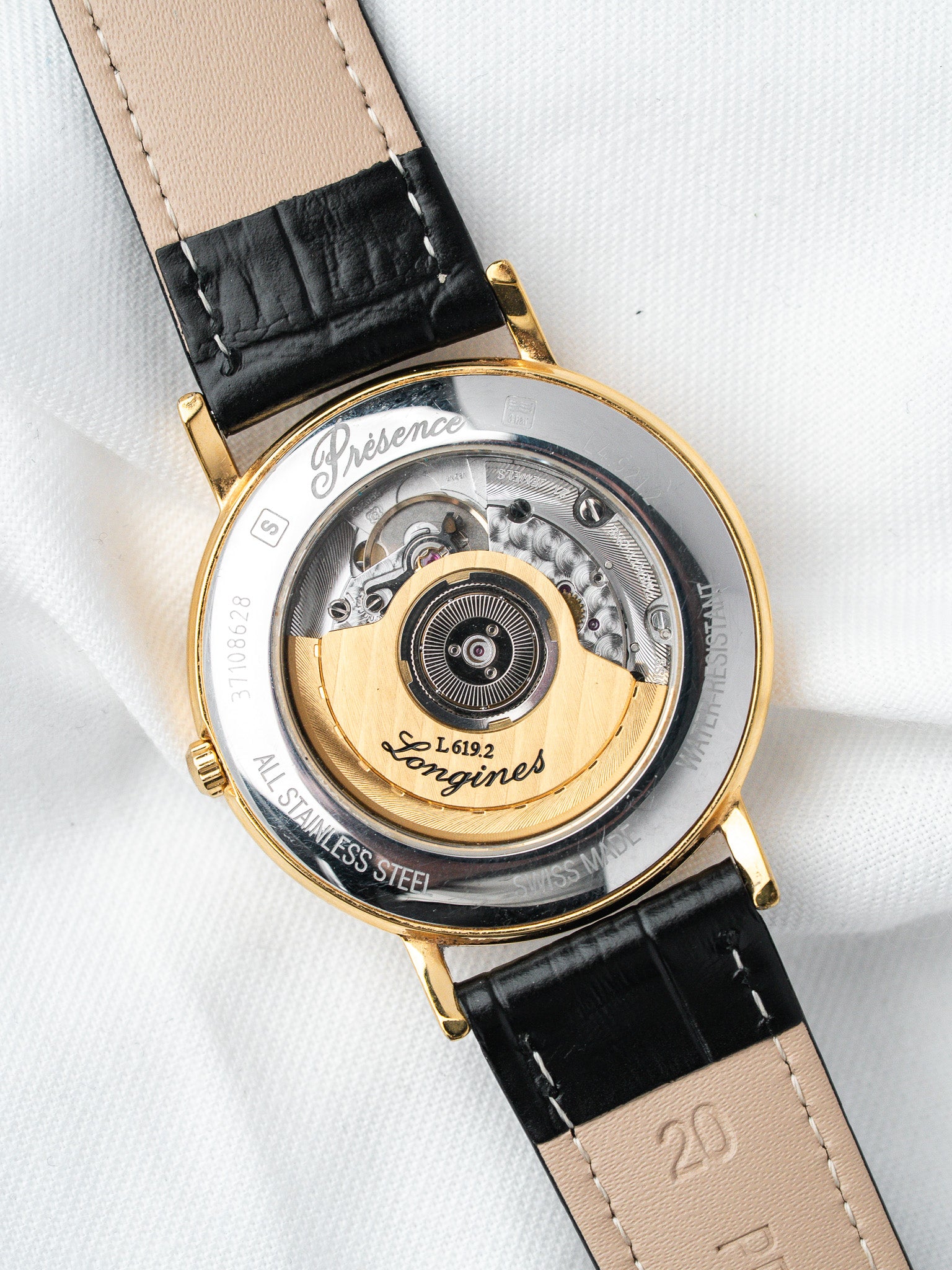 Longines Présence watch with visible mechanical movement, gold rotor, black leather strap on white background