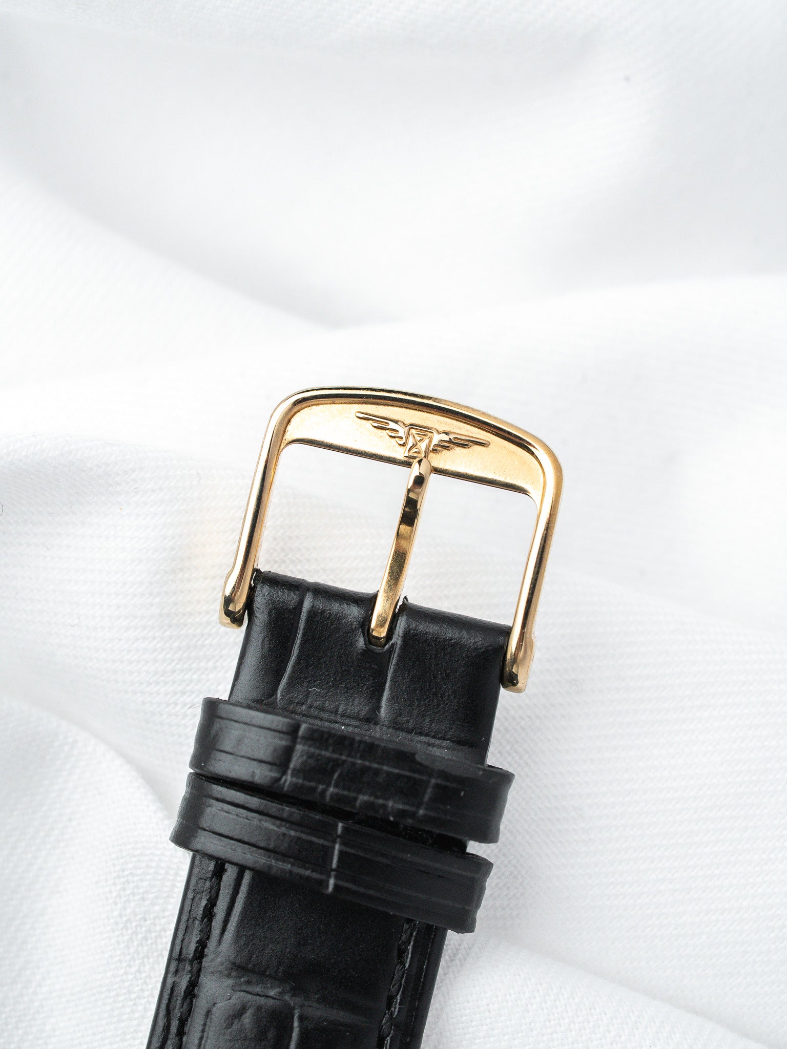 Black alligator leather strap with gold-tone buckle featuring engraved logo on white fabric