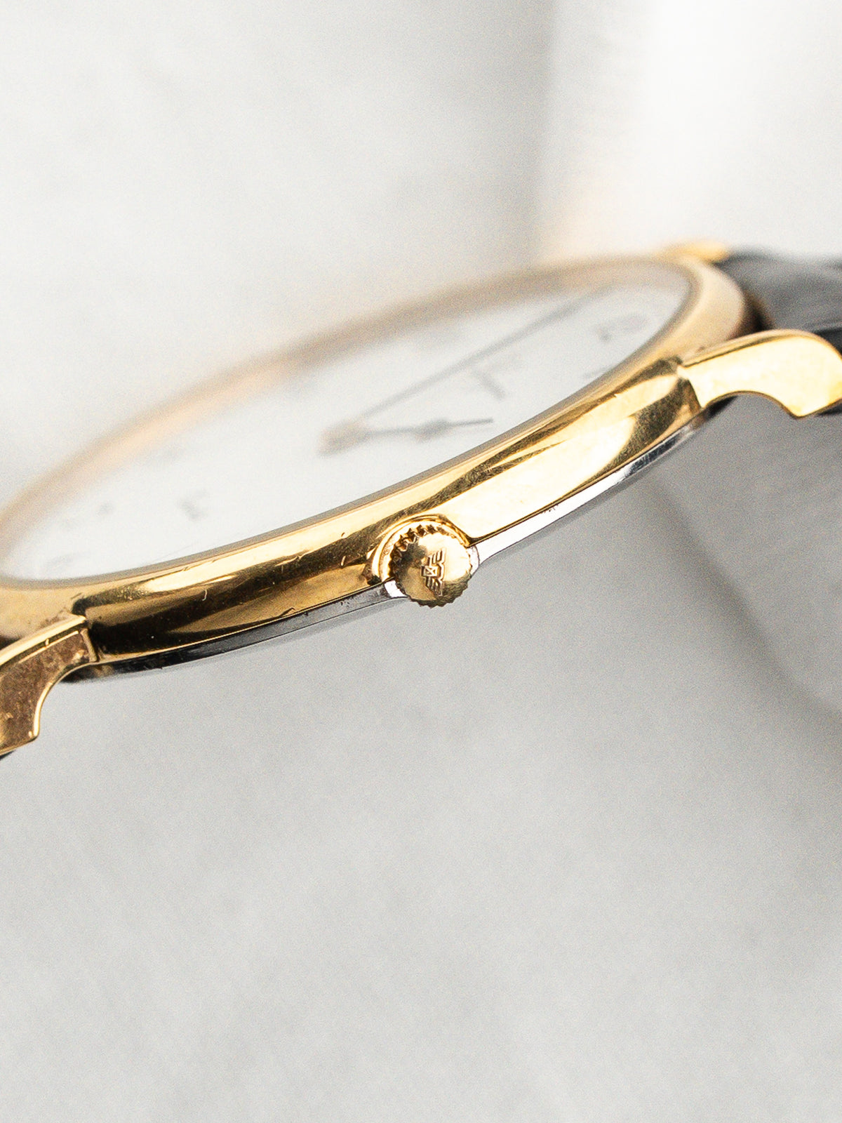 Vue rapprochée du profil d'une montre dorée avec un cadran blanc et bracelet noir.