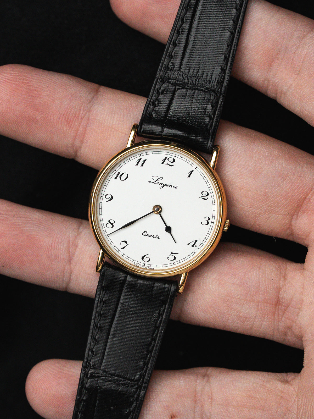Montre Longines vintage avec cadran blanc, boîtier doré et bracelet en cuir noir.