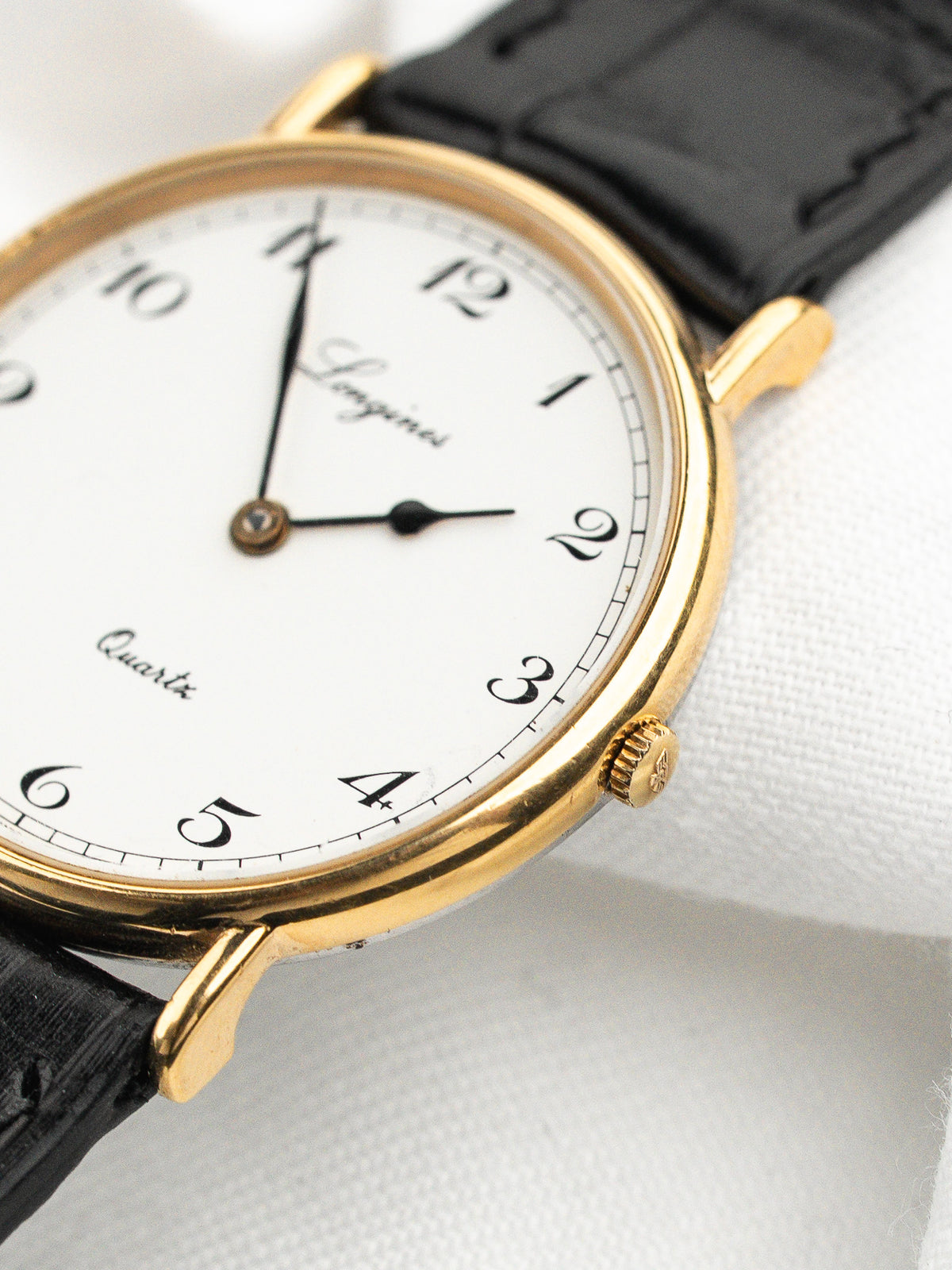 Montre Longines vintage avec cadran blanc, boîtier doré et bracelet en cuir noir.