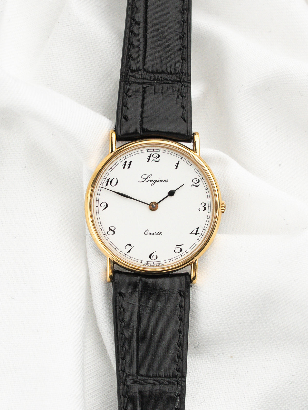 Montre Longines vintage au cadran blanc et bracelet en cuir noir texturé.