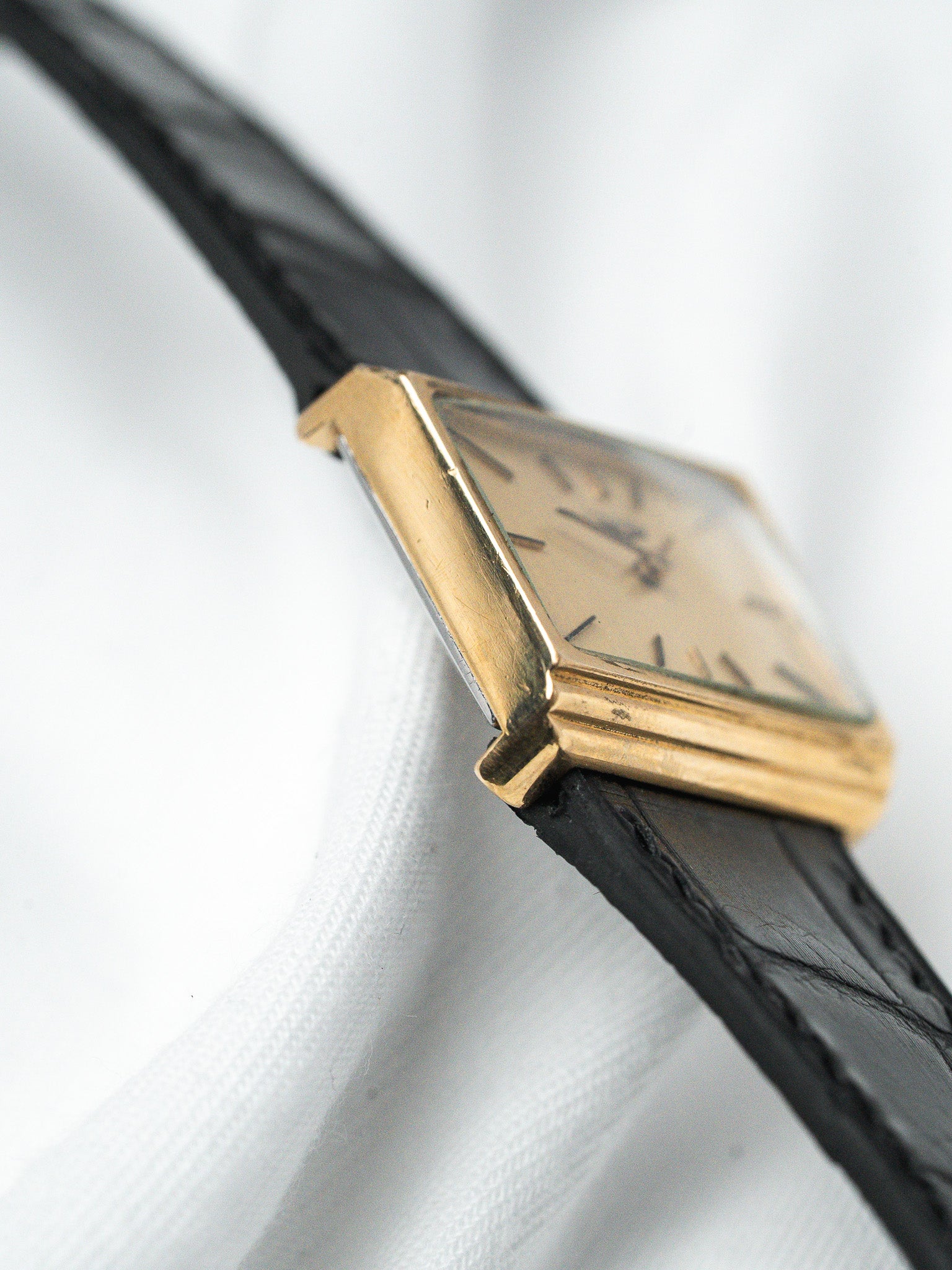 Vintage Cartier Tank watch with gold case, black leather strap, cream dial on white fabric