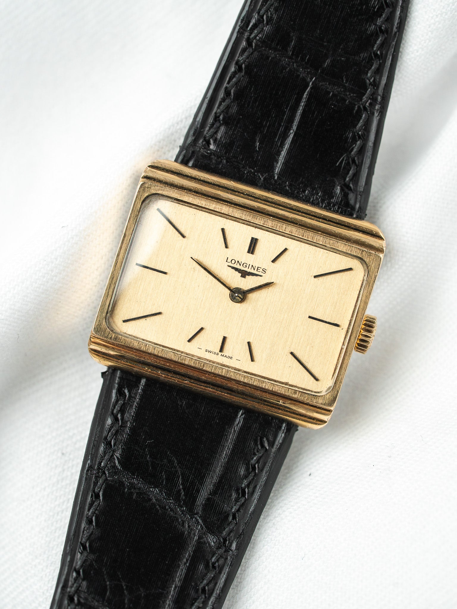 Longines vintage watch with gold case, cream dial, black alligator strap on white background