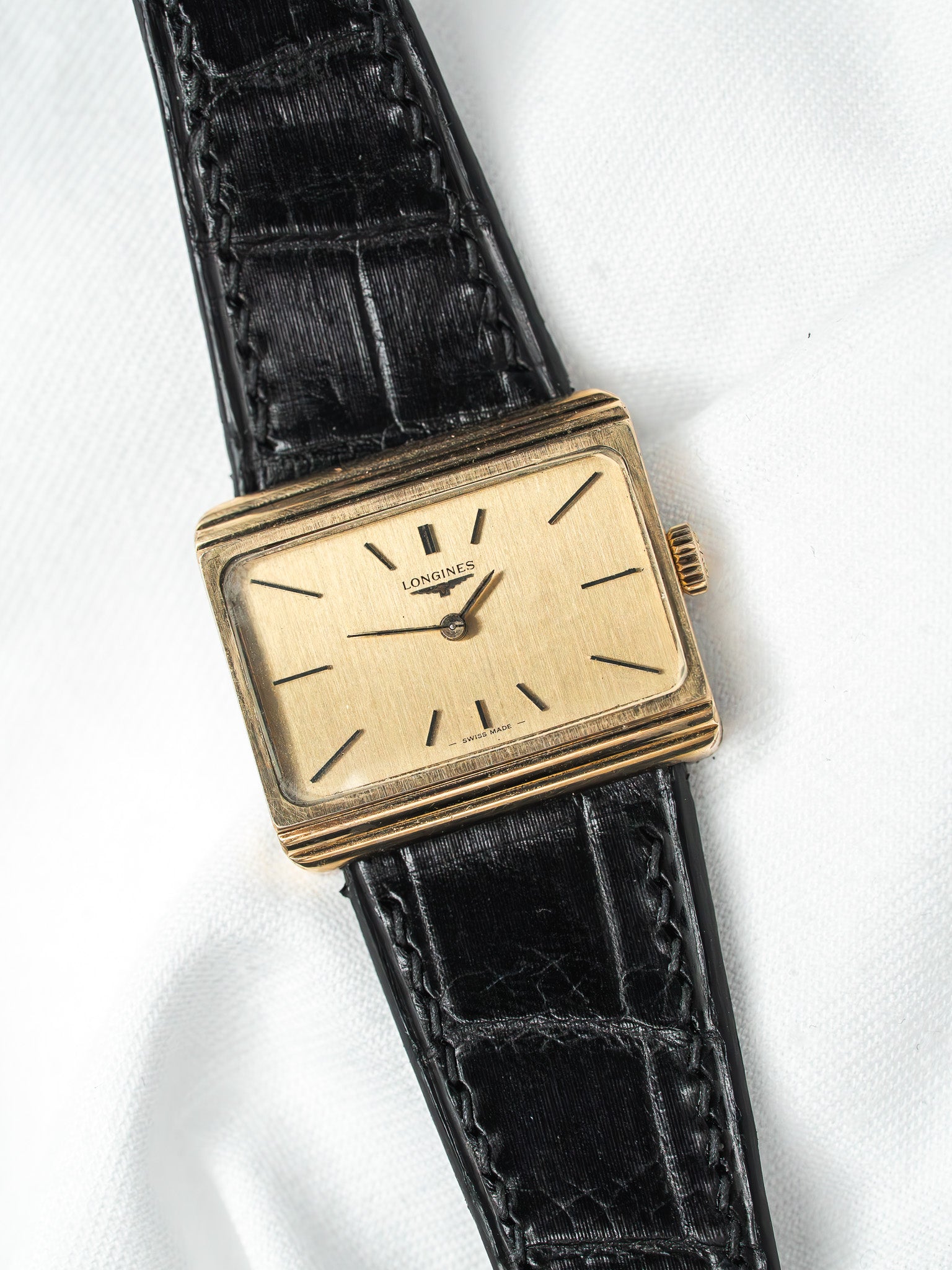 Longines vintage watch with gold case, cream dial, black alligator strap on white background