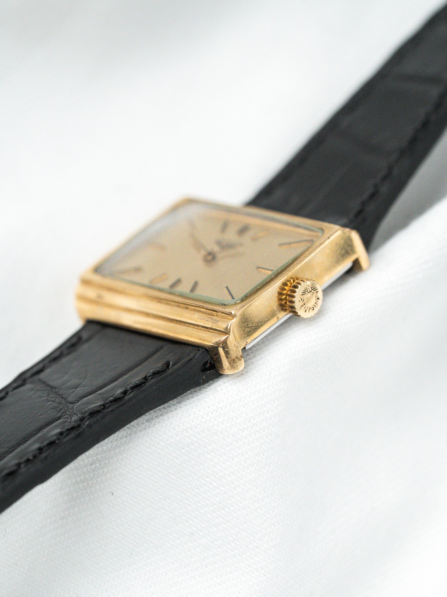 Vintage Universal Genève square gold watch with black leather strap on white background