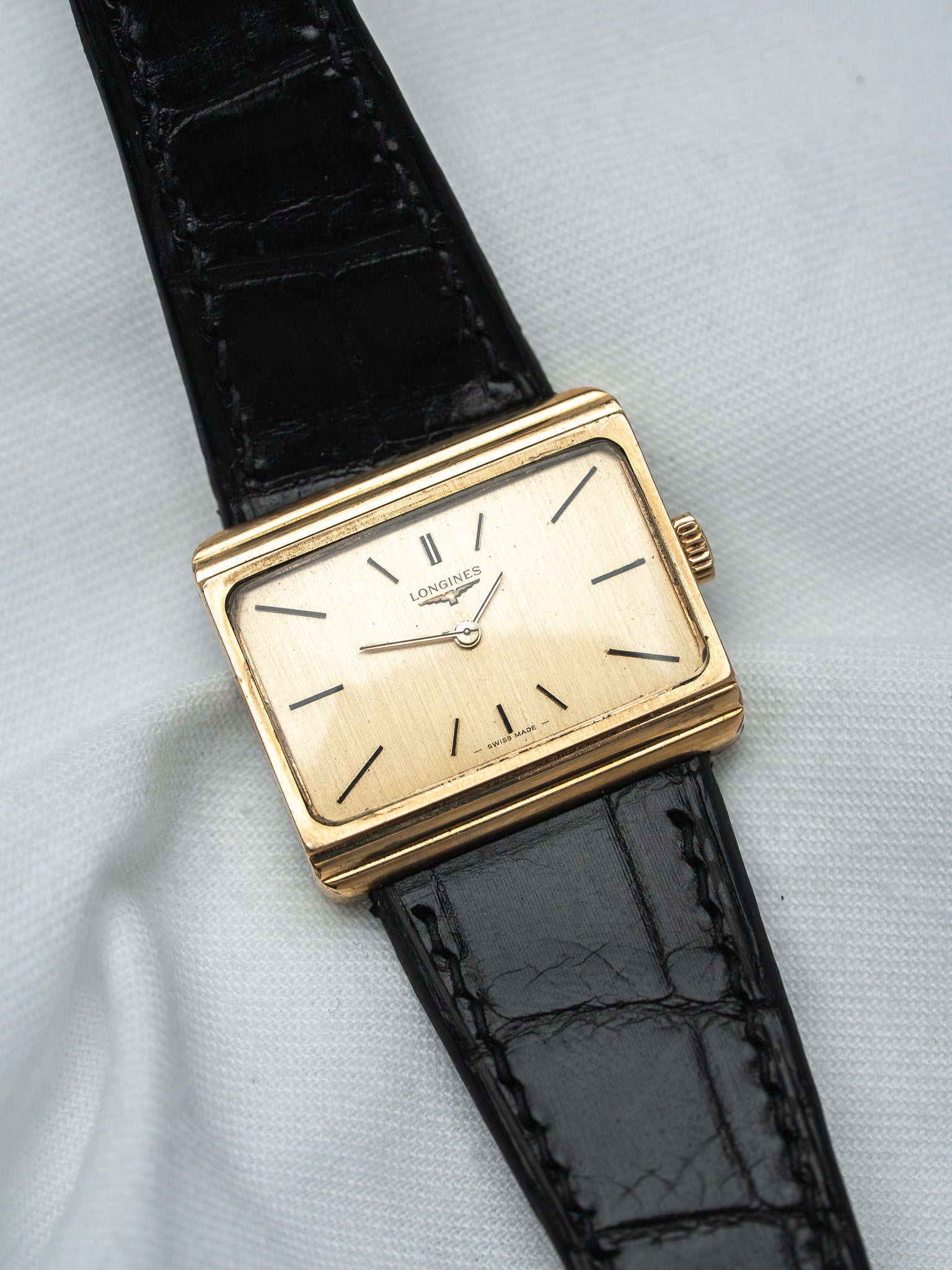 Longines vintage watch with gold case, cream dial, black alligator strap on white fabric
