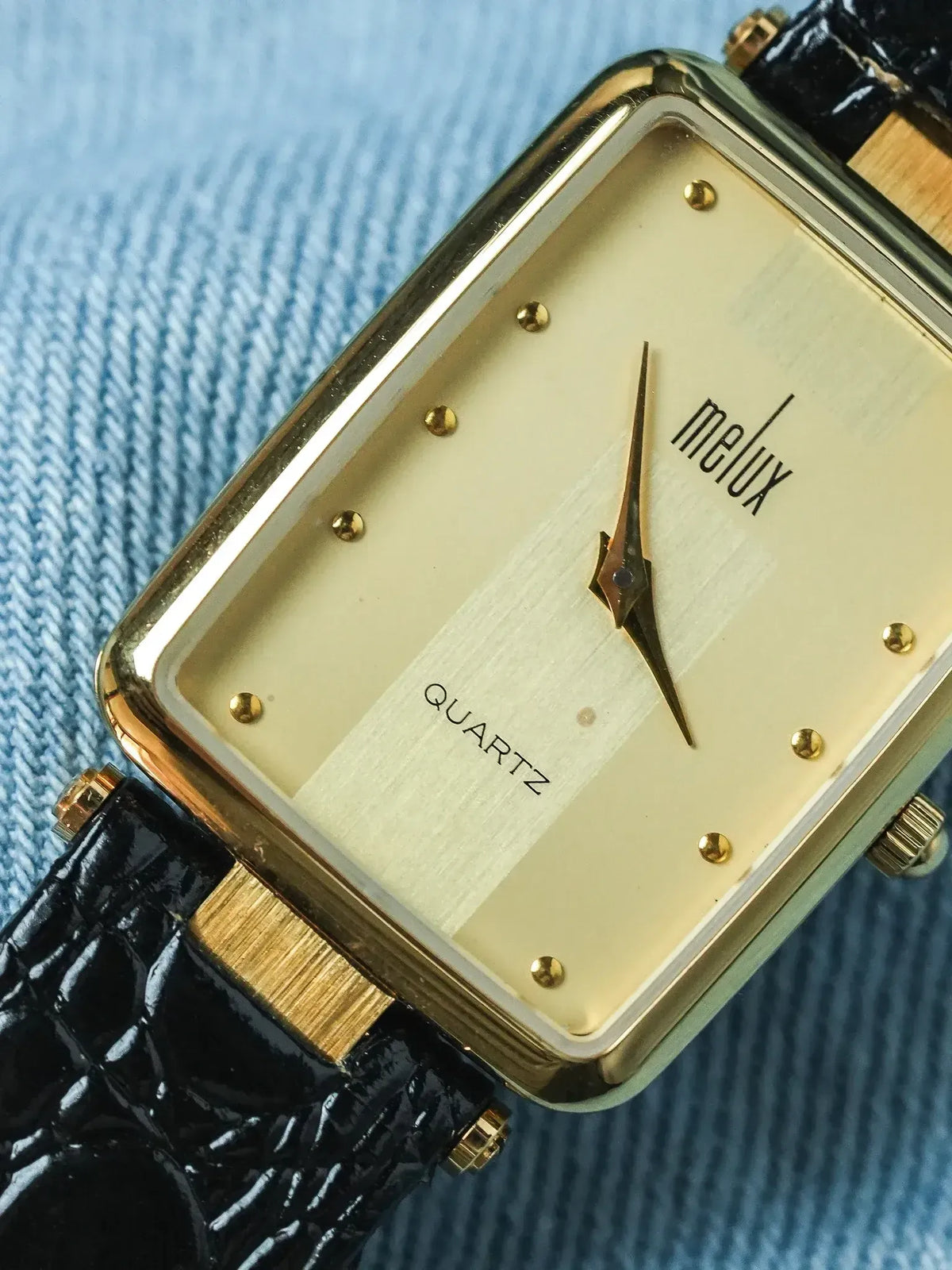 Melux vintage quartz watch, gold case, cream dial, black leather strap on denim