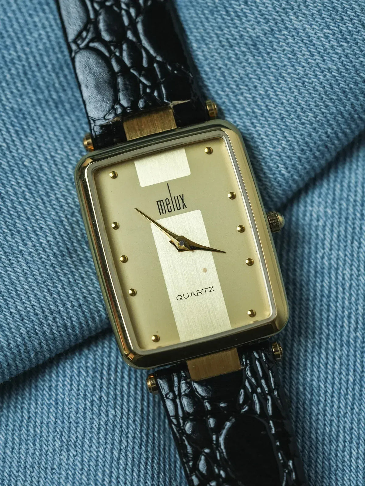 Melux vintage quartz watch with gold case, cream dial, black alligator strap on denim